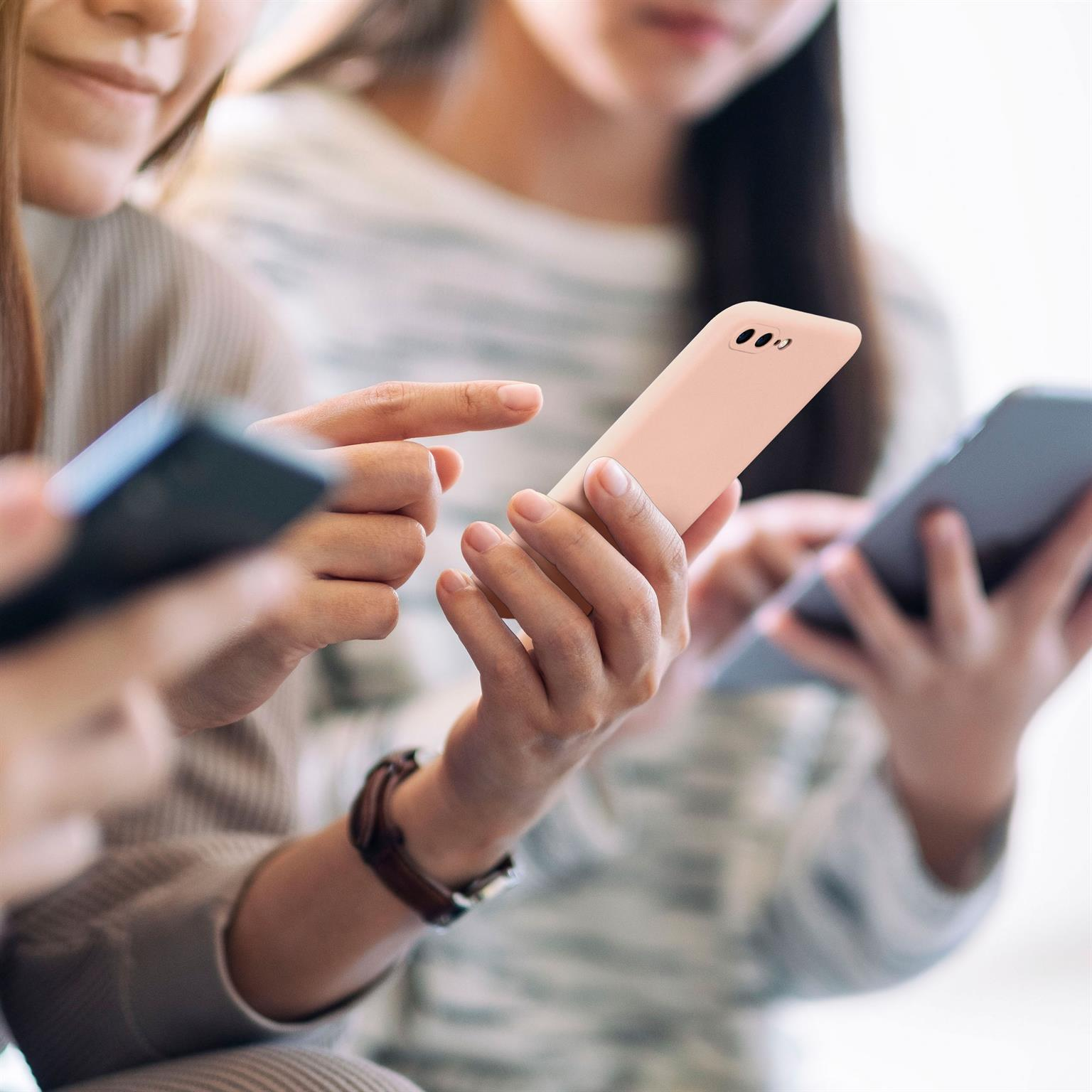 Drei Personen mit Handys, konzentriert auf Bildschirme. Ein Telefon in rosa Hülle wird gezeigt.