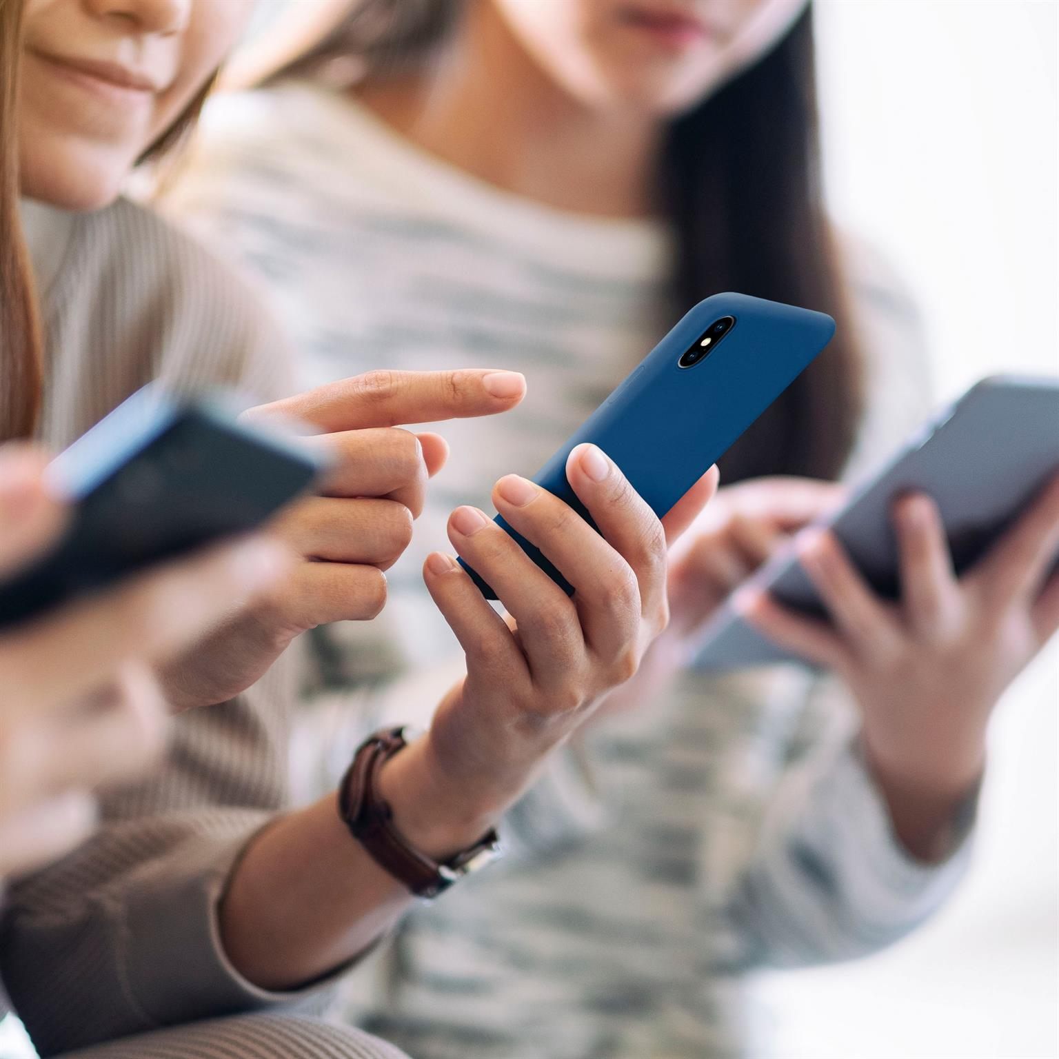 Drei Personen benutzen Smartphones. Der Fokus liegt auf Händen und Handys, mit unscharfem Hintergrund.