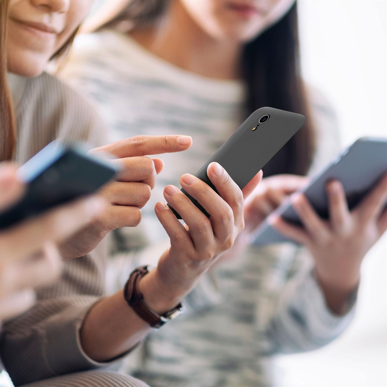 Drei Personen halten Telefone. Die Telefone sind schwarz, der Hintergrund ist unscharf.