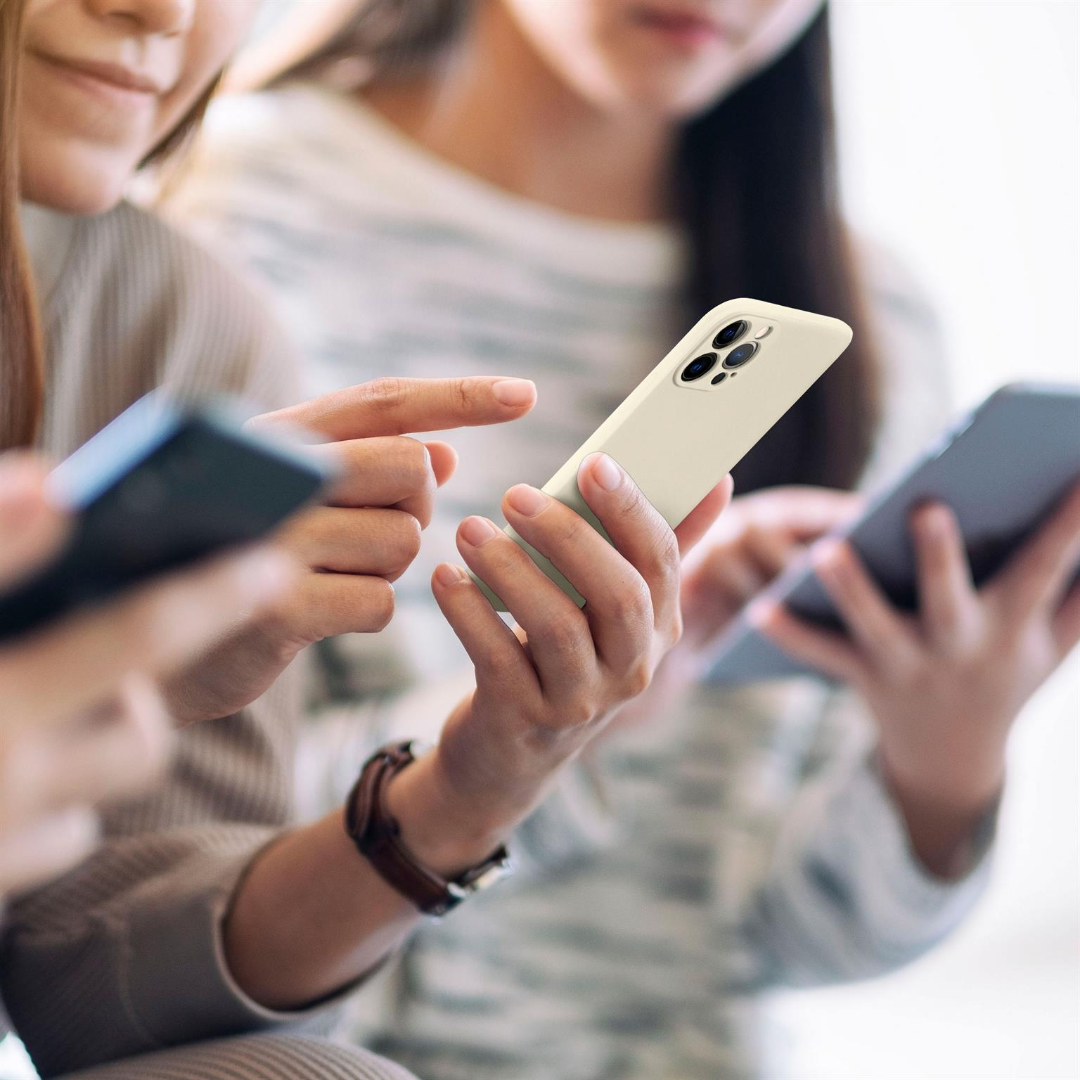Drei Personen halten Smartphones; eines mit cremefarbener Hülle, andere mit schwarzen. Hände sichtbar.