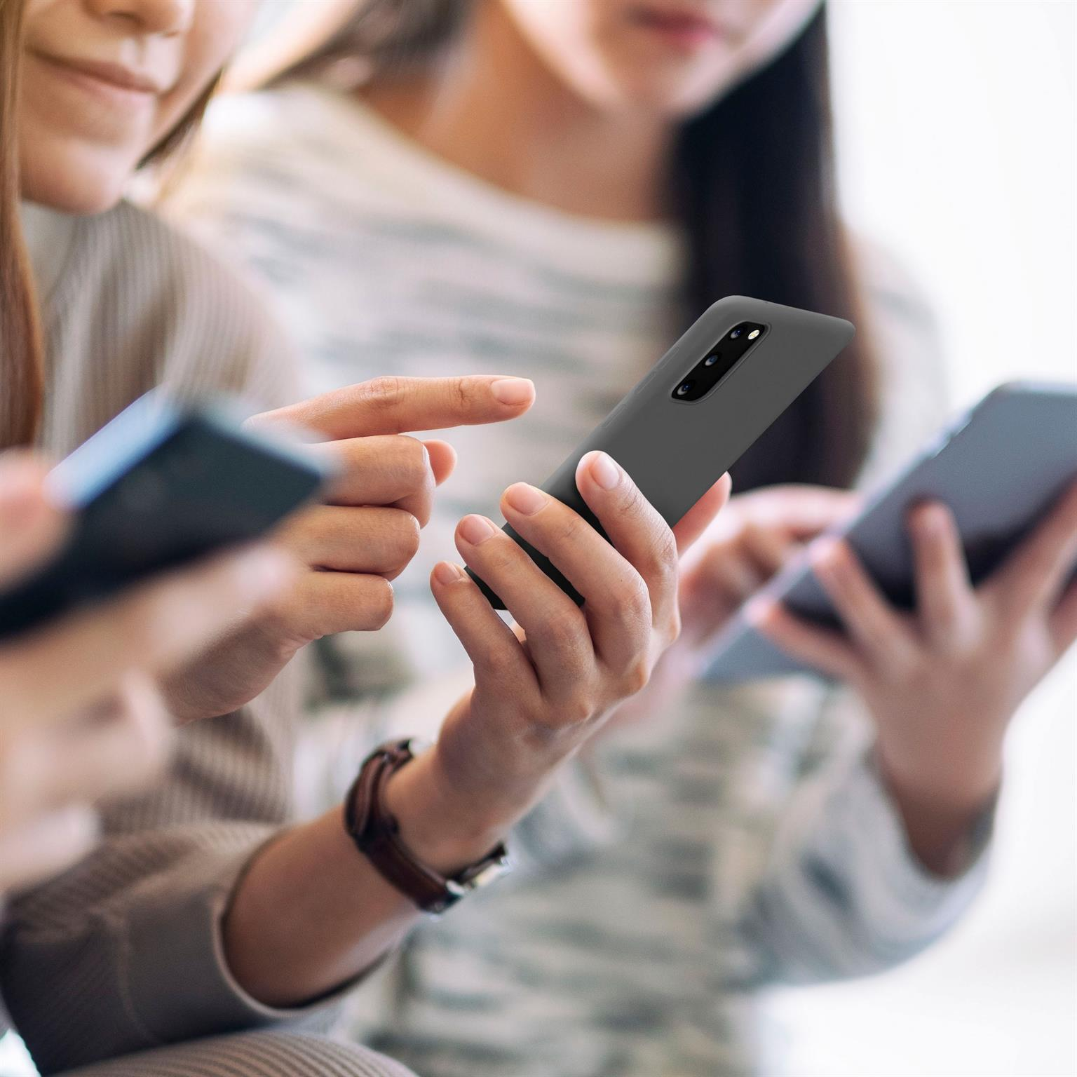 Drei Frauen halten Telefone. Ein Telefon ist rosa, eines schwarz und eines grau. Der Hintergrund ist verschwommen.
