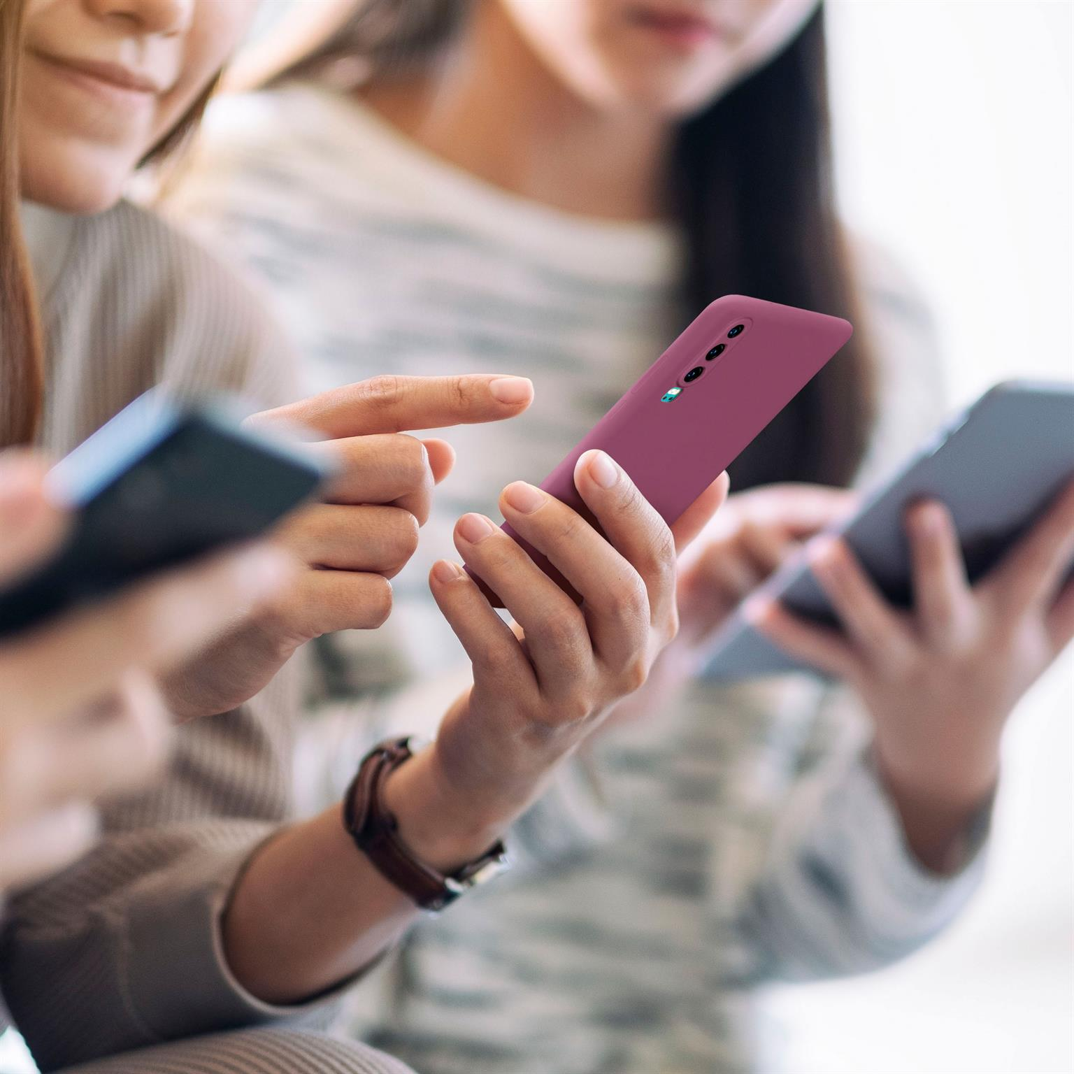 Drei Personen mit Handys, eine hält ein dunkelrotes Telefon.