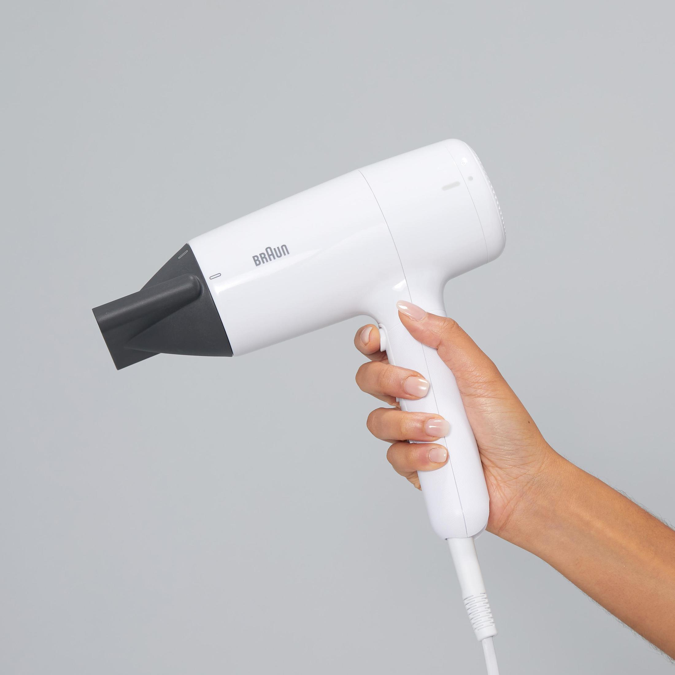 Mano di donna che tiene un asciugacapelli bianco. Sfondo grigio.