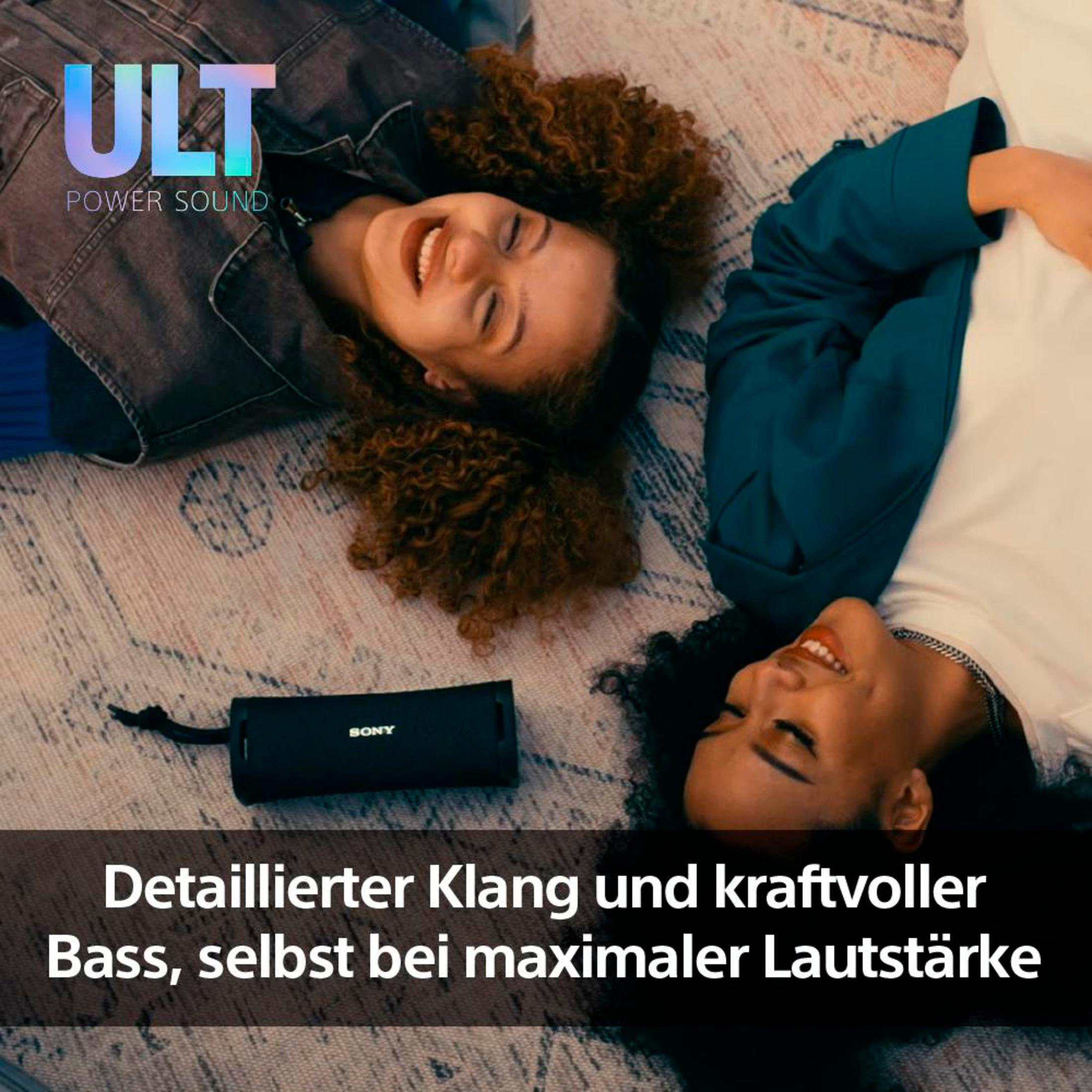 Zwei Frauen lächeln und liegen auf einem Teppich, neben einem schwarzen Lautsprecher. Text auf dem Lautsprecher.