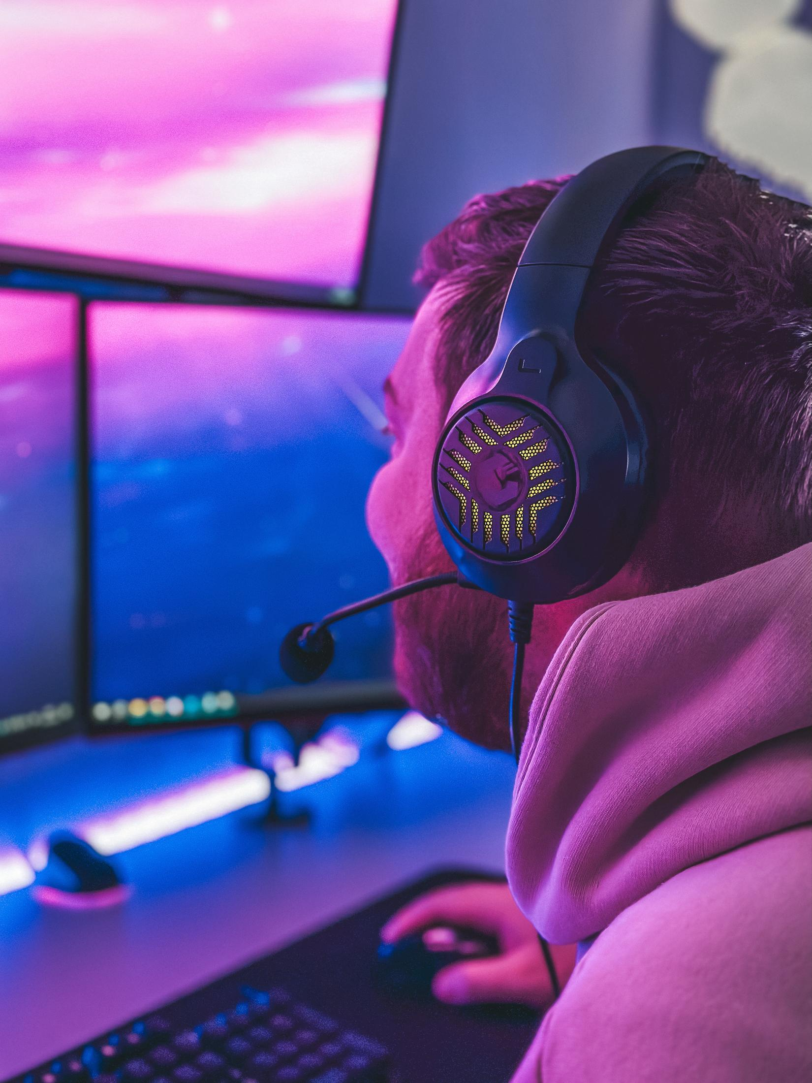 A person wearing headphones and looking at multiple computer screens.