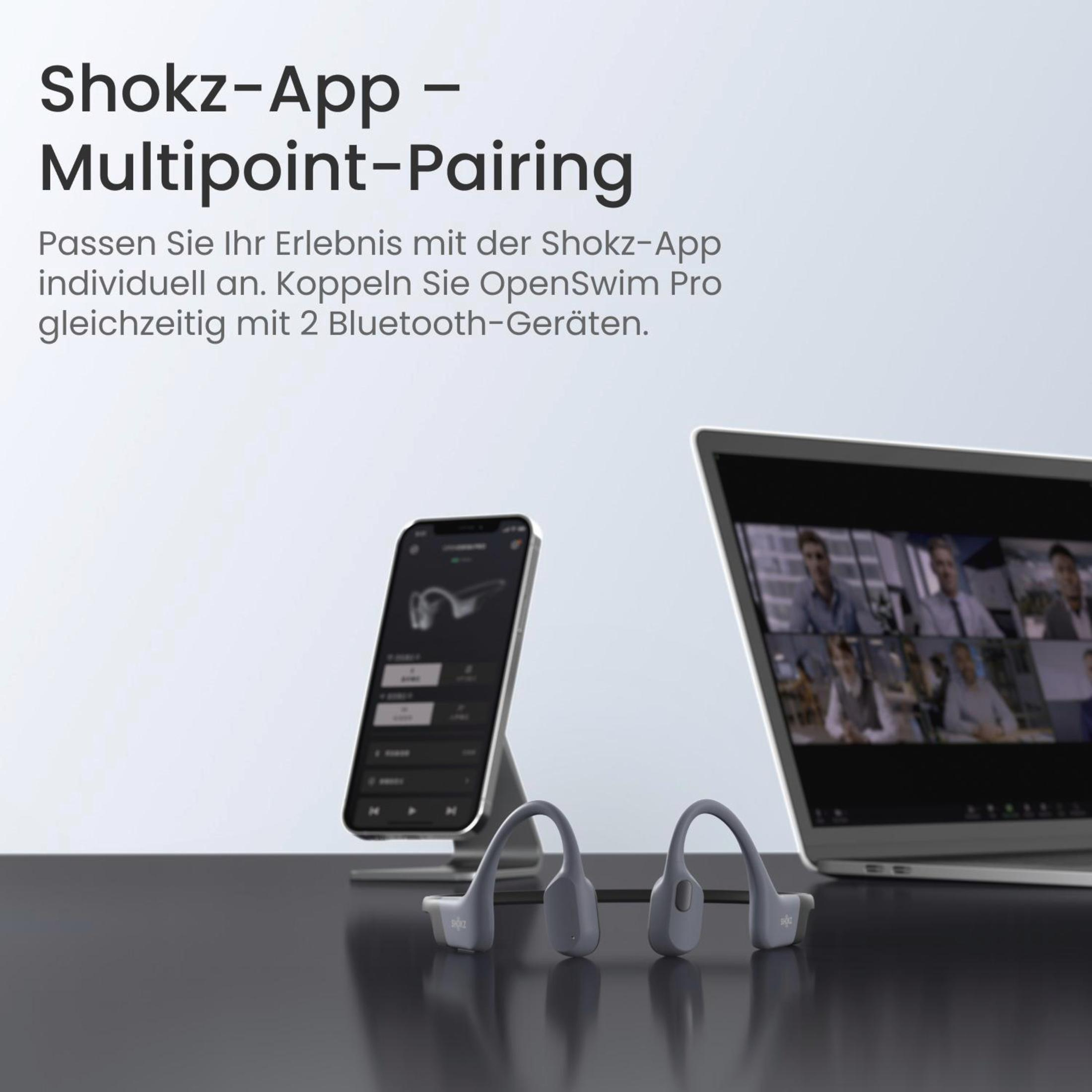 Cuffie Shokz, telefono e laptop. Le cuffie sono grigie. Il telefono mostra le cuffie. Il laptop mostra una videochiamata.
