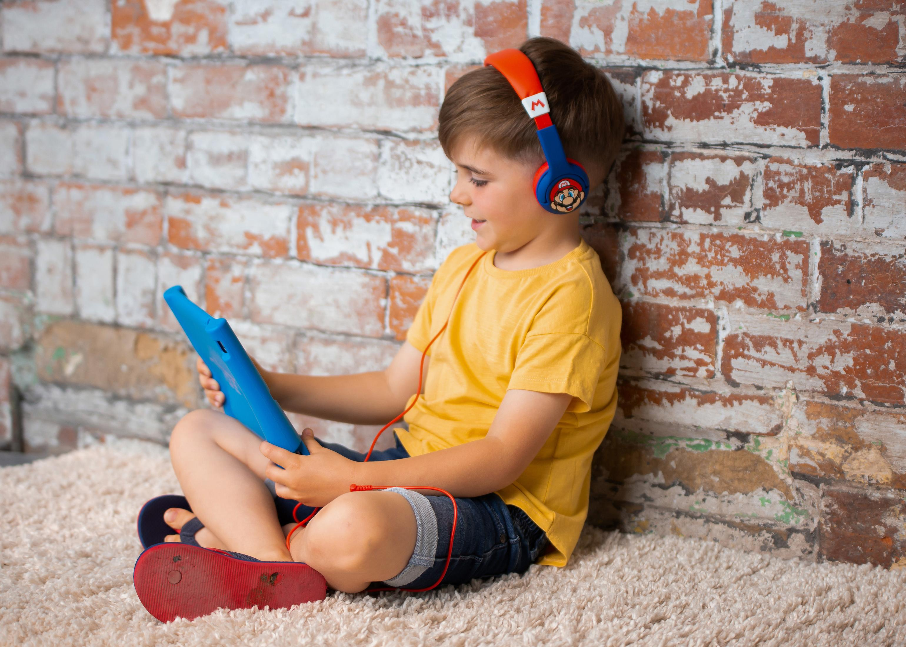 Chłopiec ze słuchawkami Mario siedzi na dywanie, używając niebieskiego tabletu.