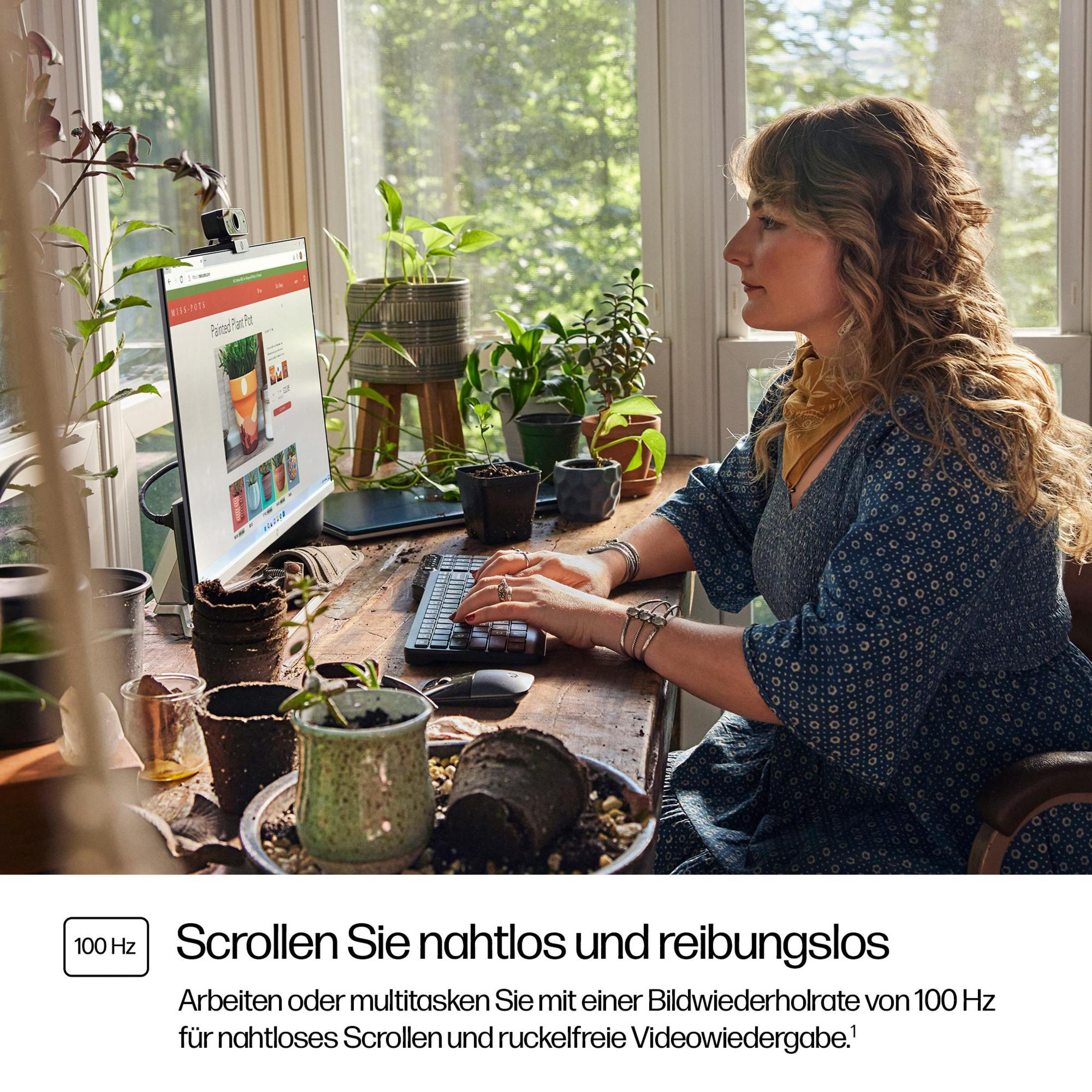 Kobieta pracująca na komputerze przy oknie. Na ekranie wyświetlana jest strona internetowa z roślinami.