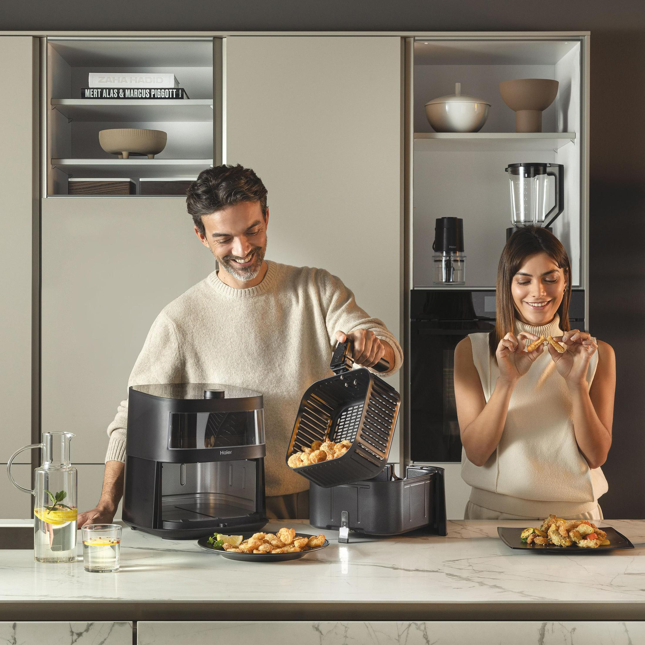 Dwie osoby w kuchni, jedna z frytkownicą powietrzną, a druga jedząca jedzenie.
