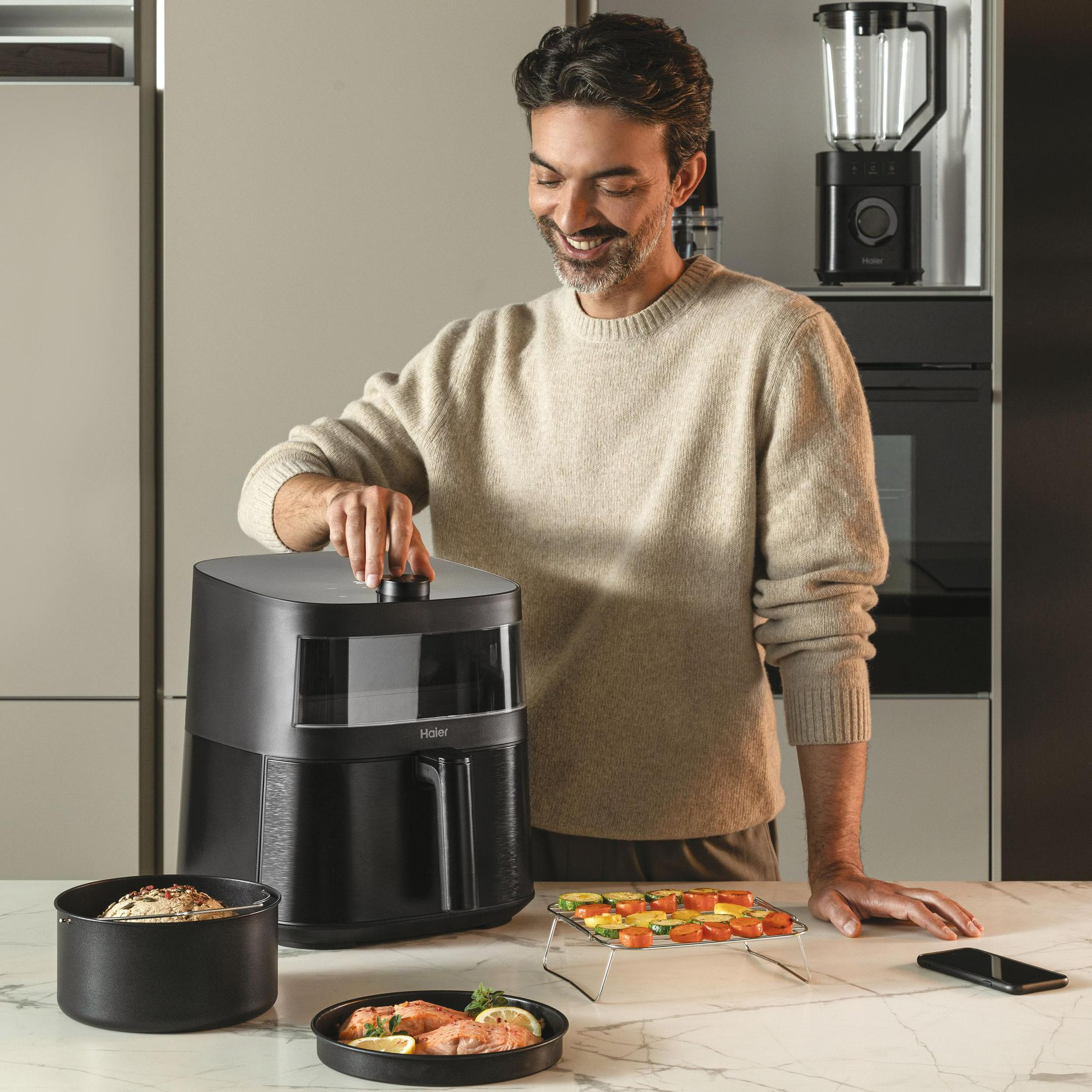 Mężczyzna używa frytownicy powietrznej. W tle znajdują się produkty spożywcze i blender.