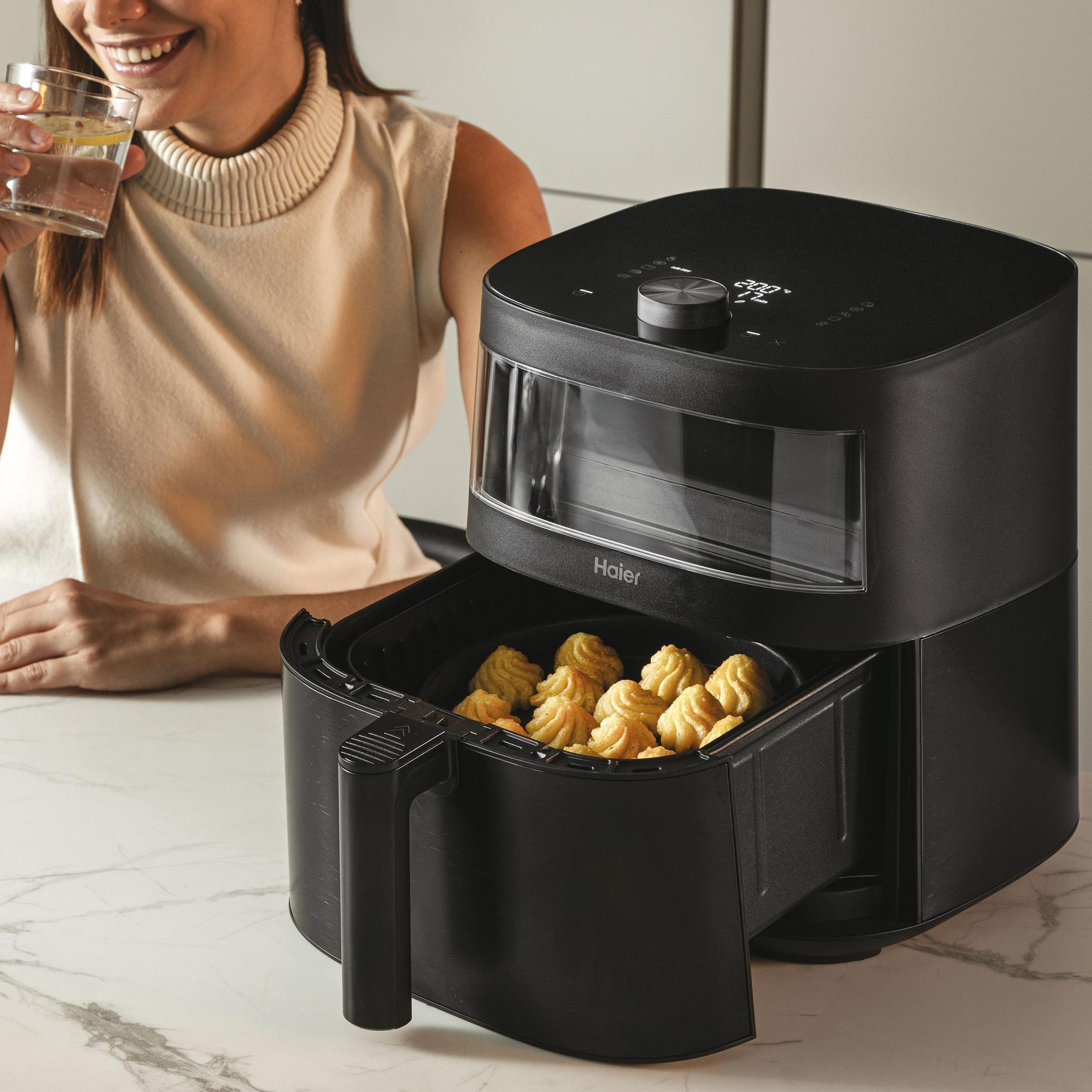 Uśmiechnięta kobieta, trzymająca szklankę. Czarna frytkownica, jedzenie w koszu.