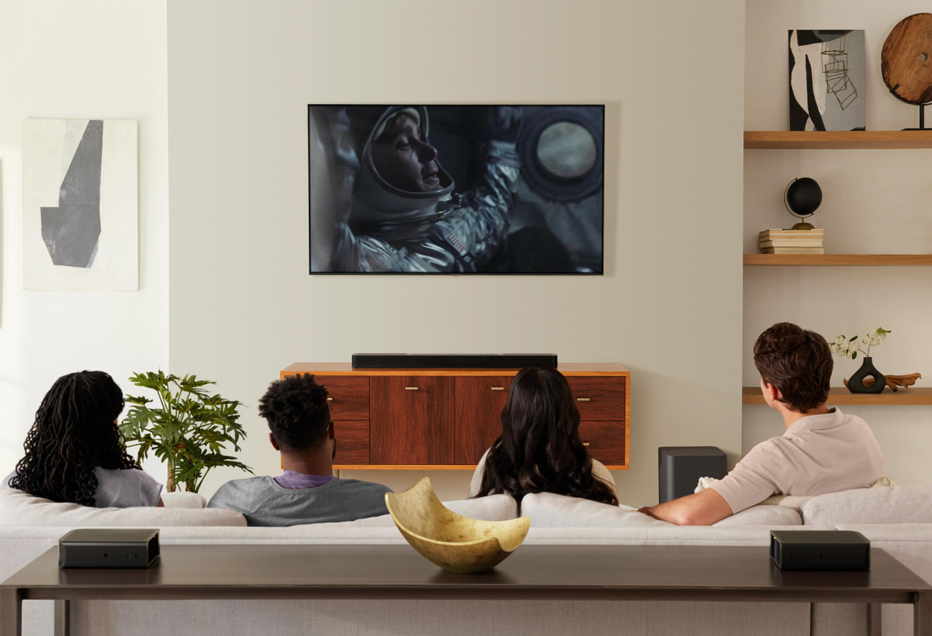 Bir film gösteren bir TV'nin olduğu bir oturma odası. İnsanlar bir kanepede TV izliyor.