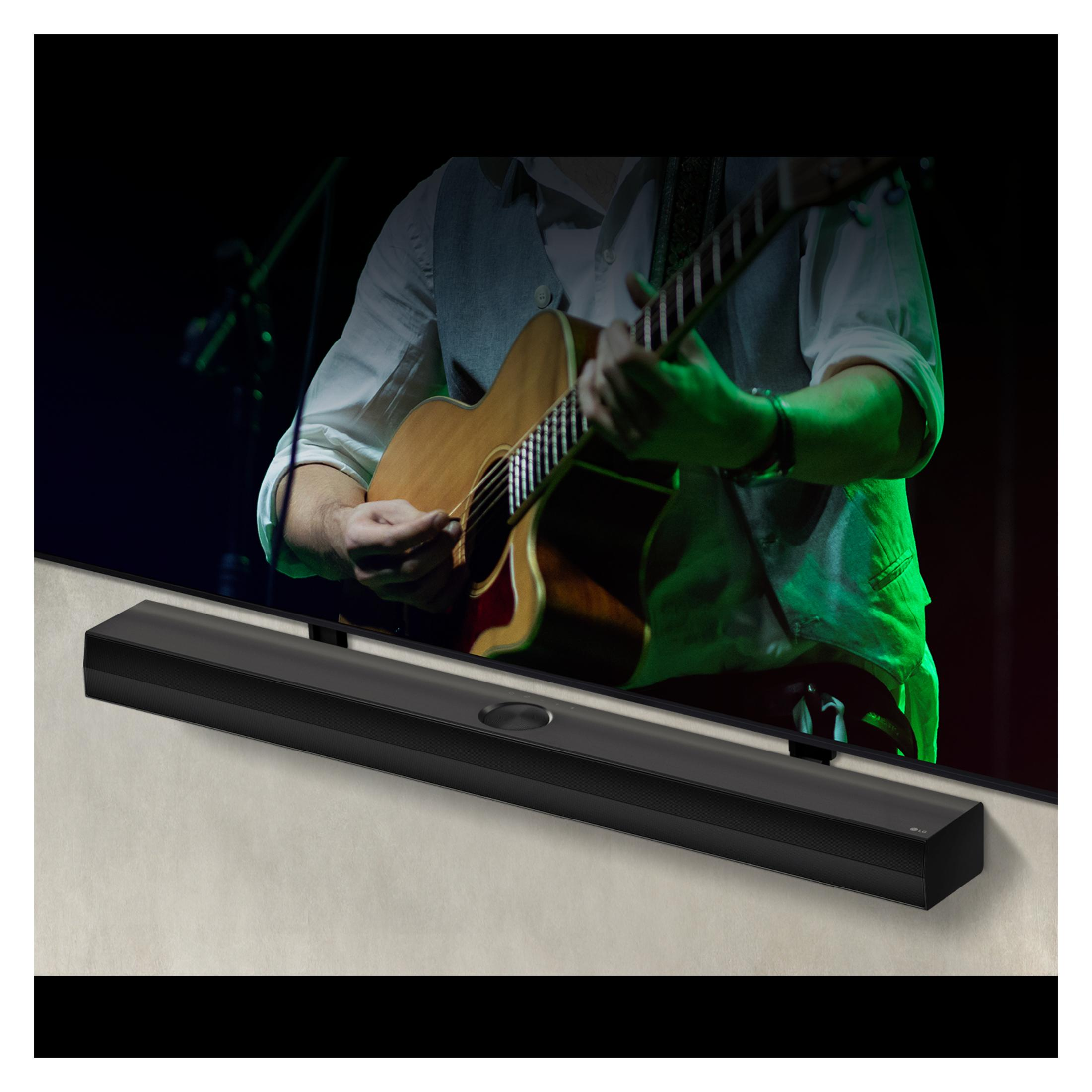 Czarny soundbar pod ekranem telewizora. Na ekranie mężczyzna gra na gitarze.