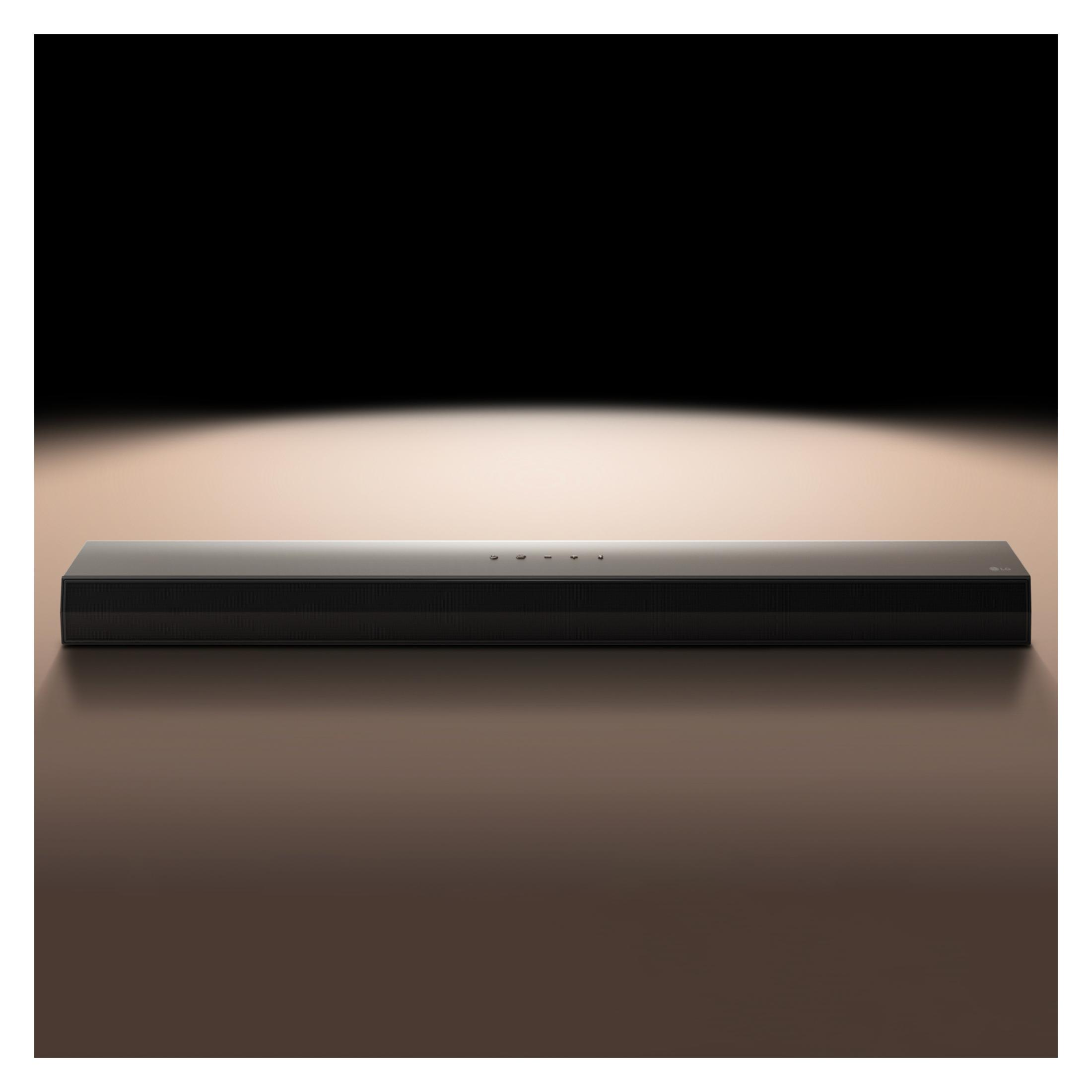 Czarny soundbar na brązowej powierzchni z reflektorem nad nim, tworzącym efekt świetlny.