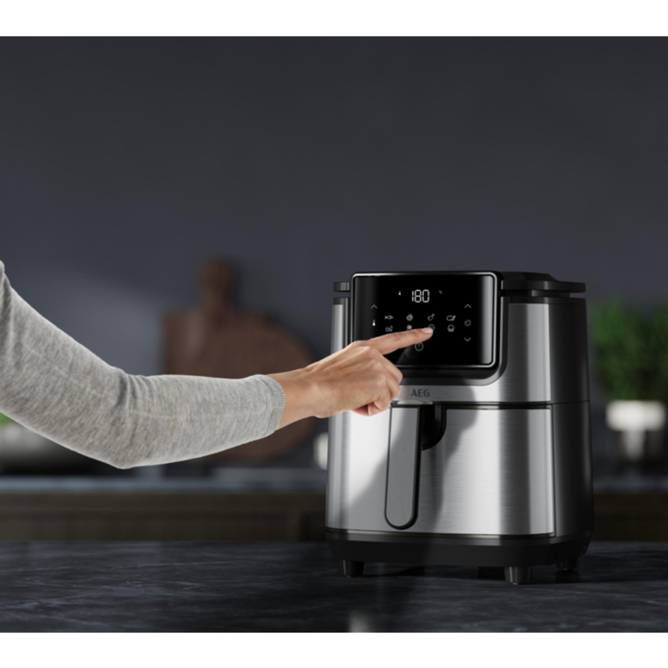 Mano preme pulsante friggitrice ad aria, mostra display e logo AEG.