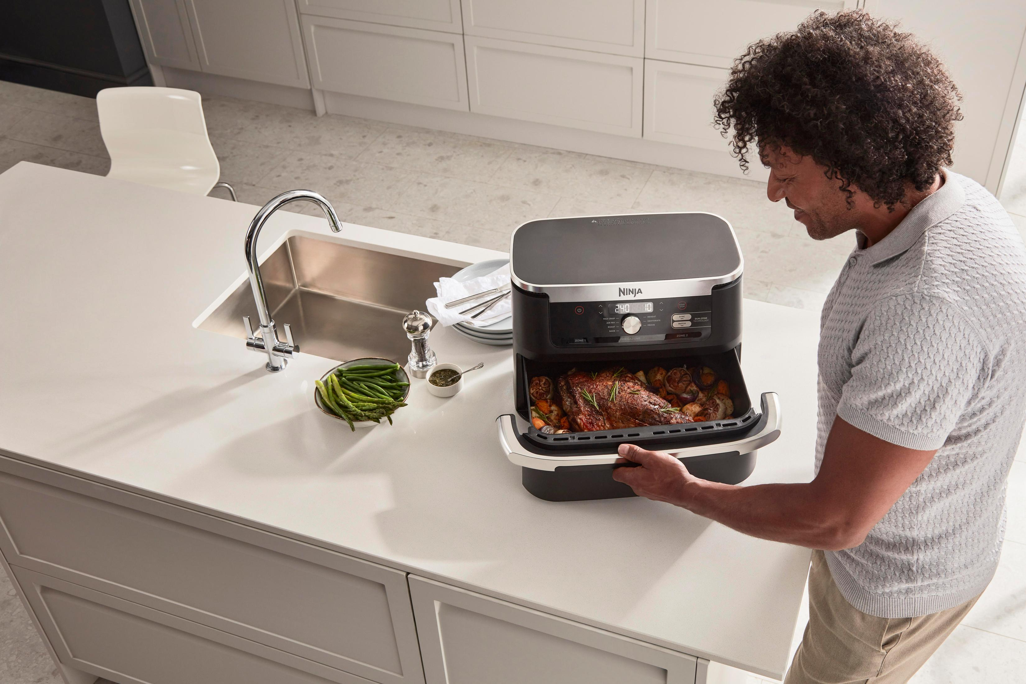 Een man in een keuken die een bak met gekookt voedsel uit een Ninja airfryer haalt.