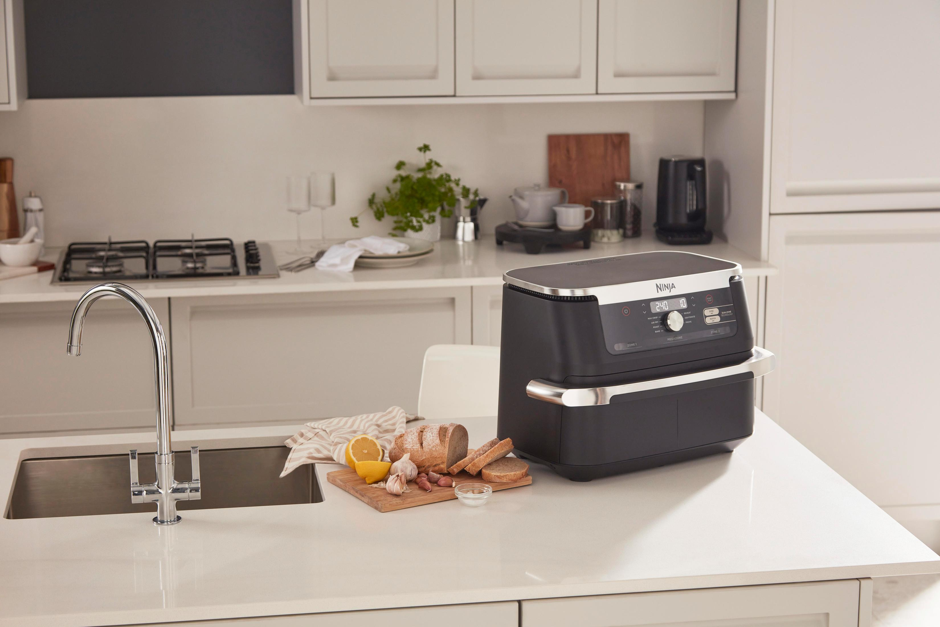Een keuken met een zwarte Ninja airfryer op een aanrecht. Brood, citroenen en knoflook liggen in de buurt.