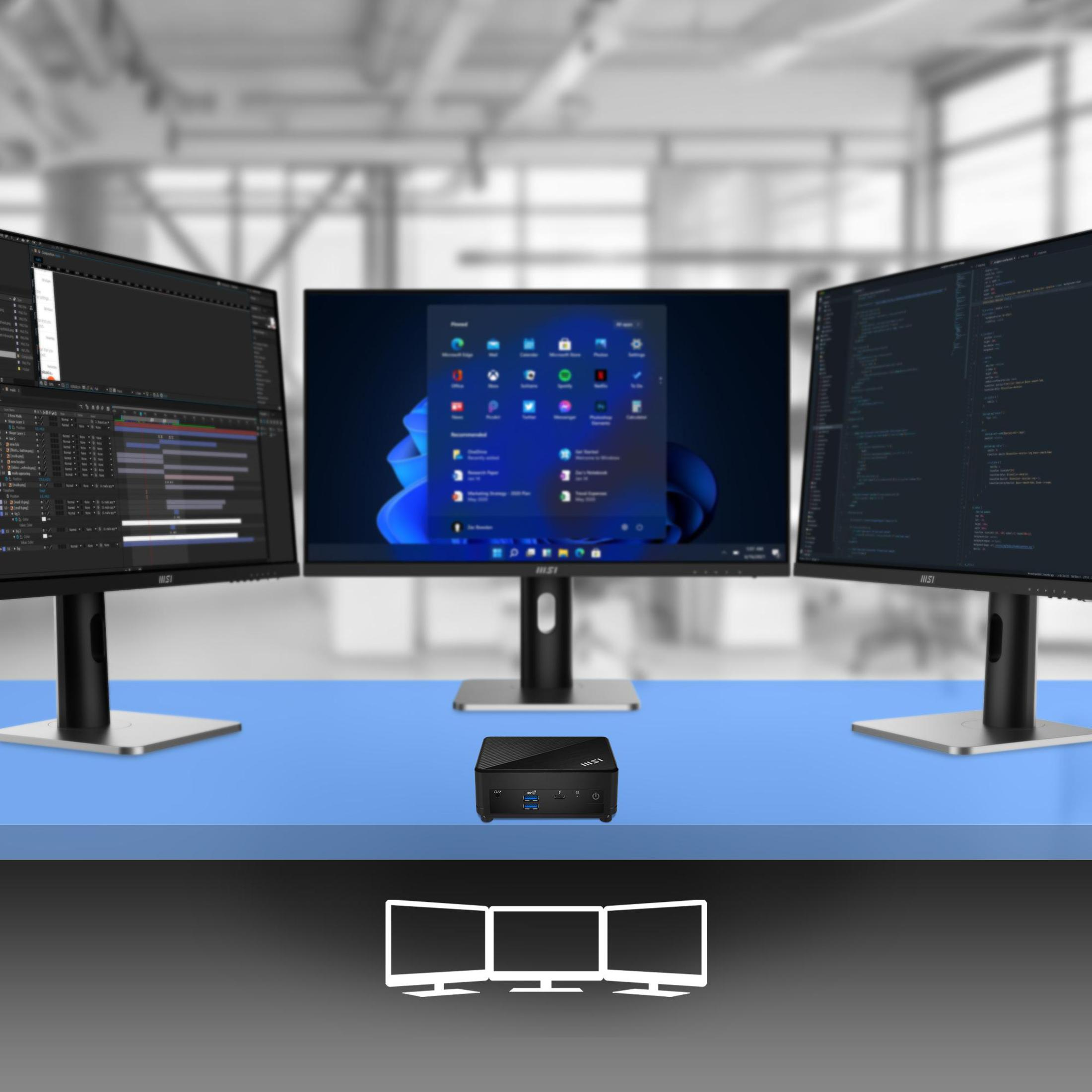 Tre monitor, un piccolo computer e una scrivania blu. Lo sfondo è un ambiente d'ufficio sfocato.