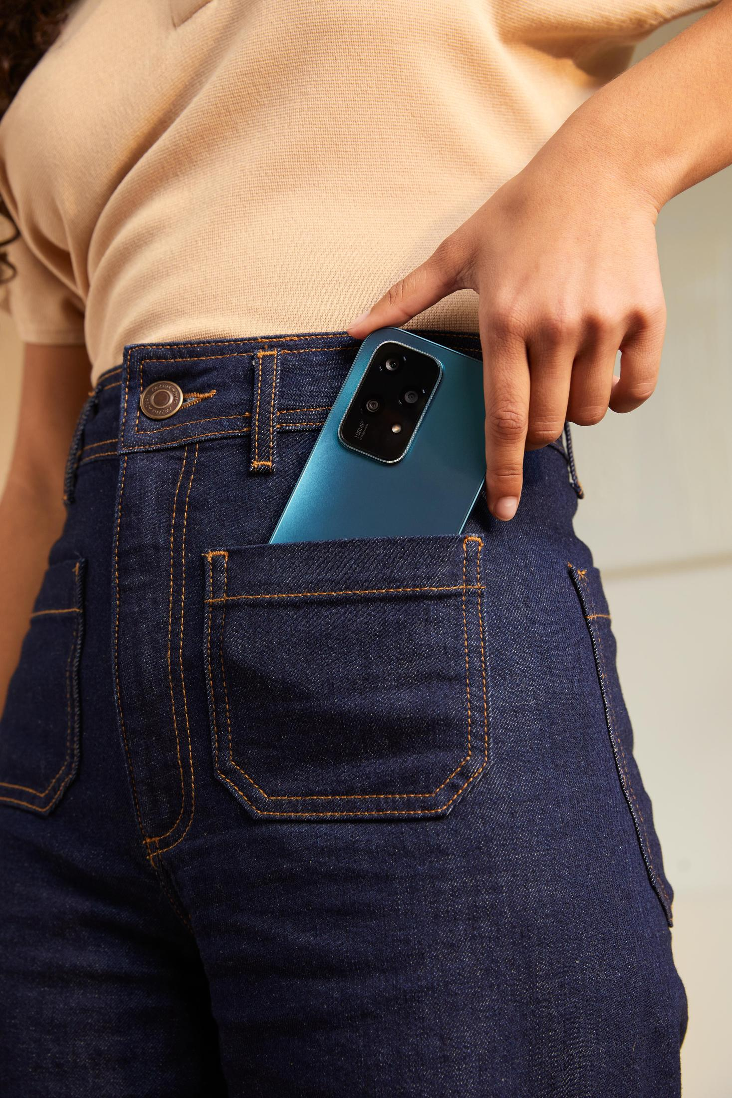 Eine Hand legt ein blaues Telefon in eine Jeans-Tasche.