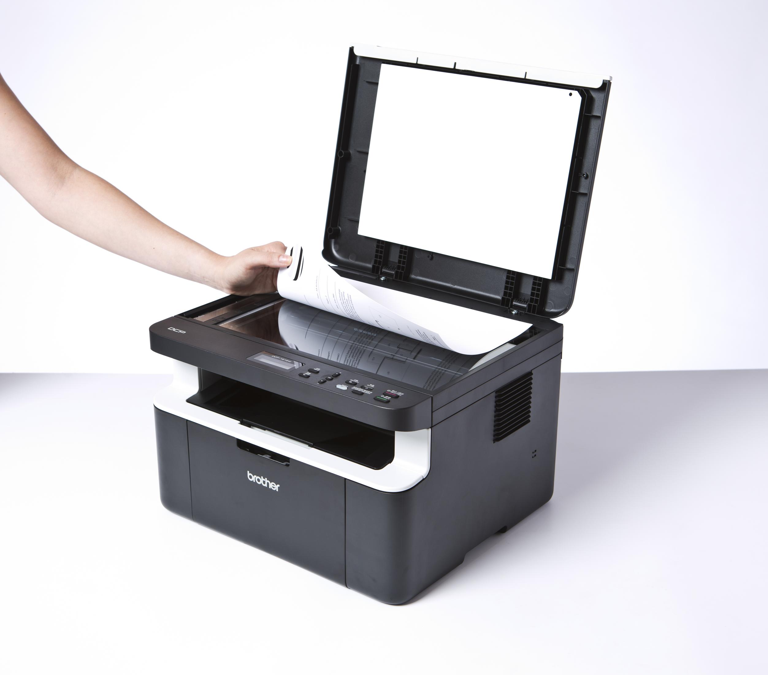 Die Hand einer Person öffnet einen Drucker. Der Drucker ist schwarz und weiß. Ein Dokument befindet sich darin.