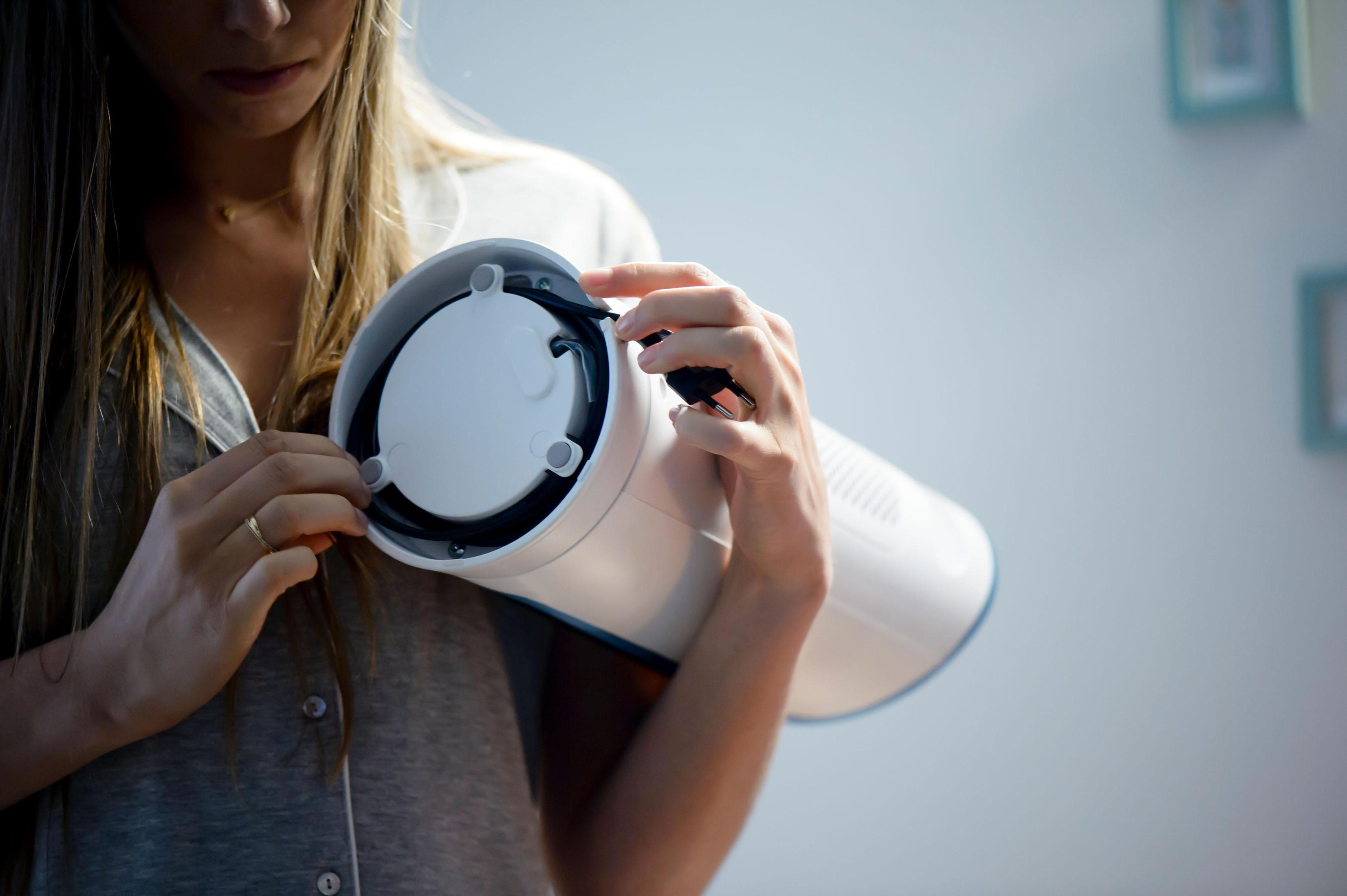 Kobieta montuje biały wentylator. Podłącza czarny kabel, jasne tło.