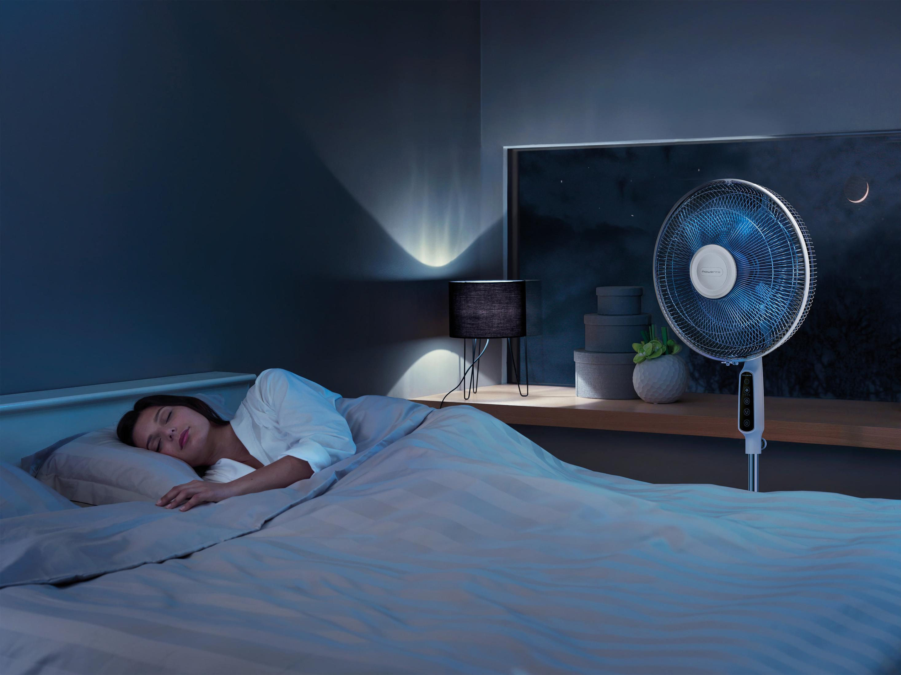 Kobieta śpiąca w łóżku z wentylatorem. Nocna scena z oknem i lampą.