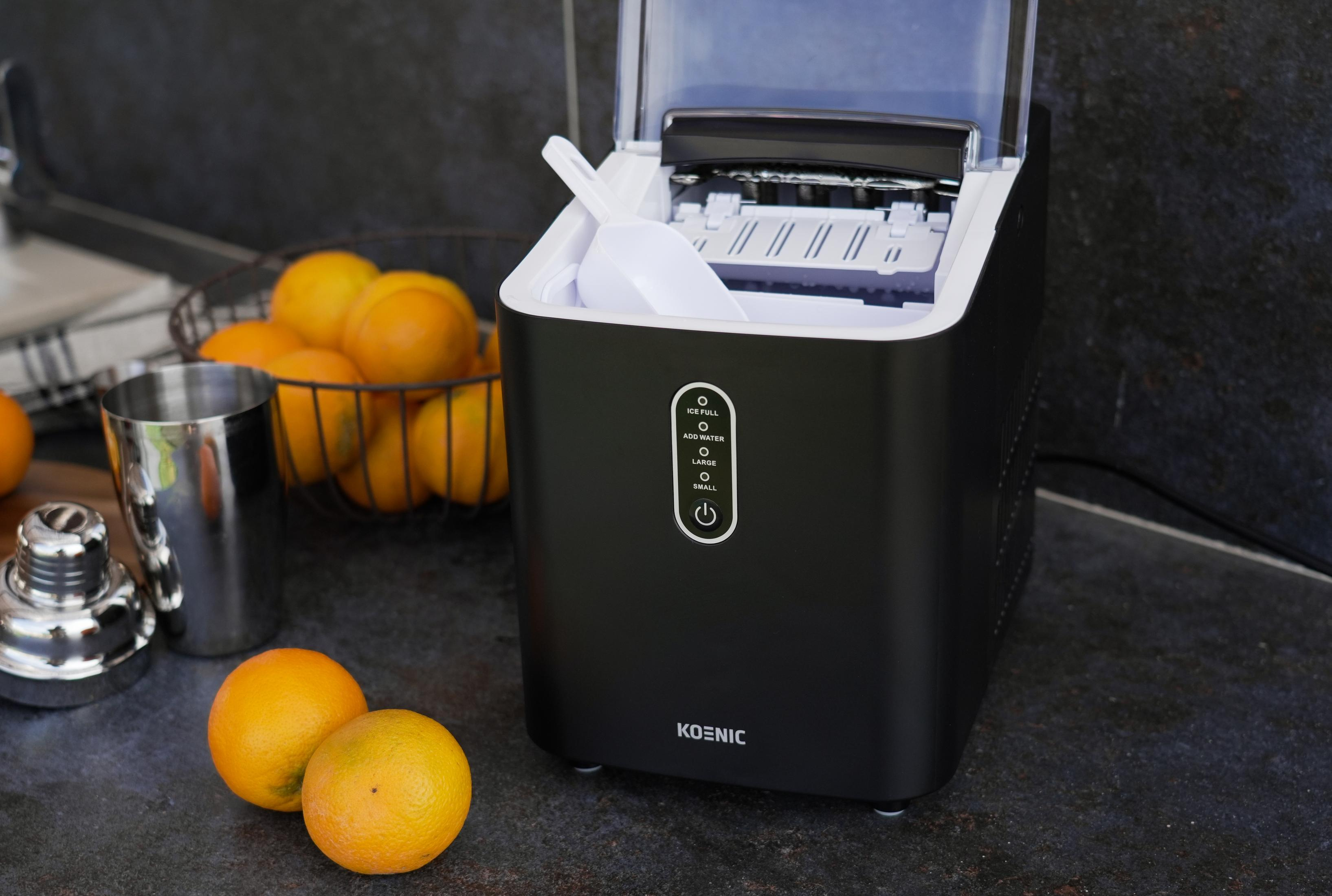 Schwarzer Eismaschine mit Orangen und Cocktailshaker auf Stein. Weißer Eisportionierer.