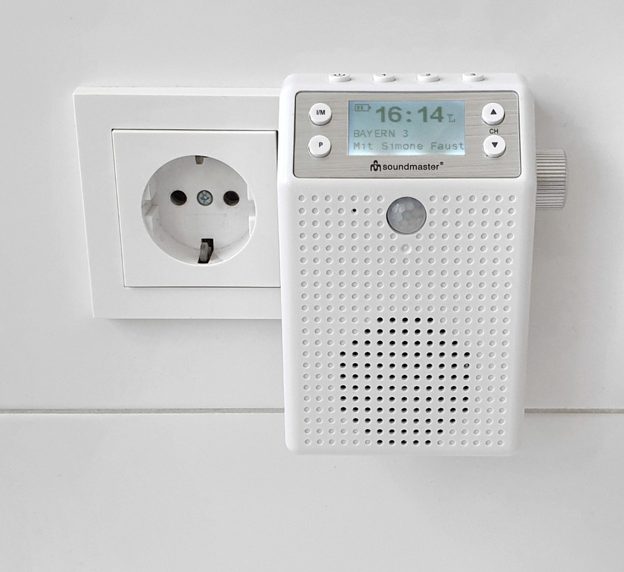 Weißes Radio, das in eine weiße Steckdose gesteckt ist. Das Radio zeigt Zeit und Sender.