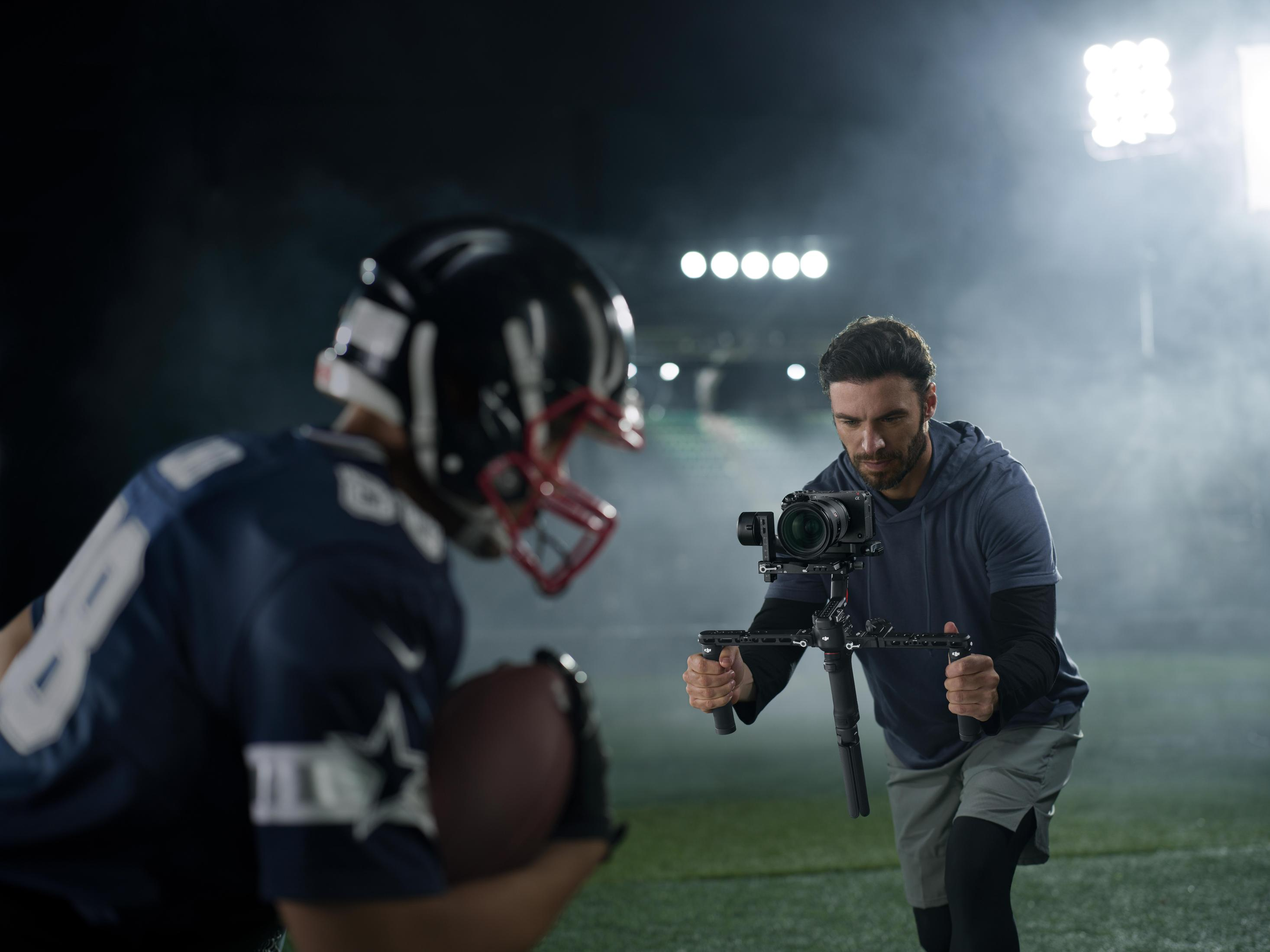 Ein Videofilmer filmt einen Footballspieler. Dunkler Hintergrund, Scheinwerfer an.