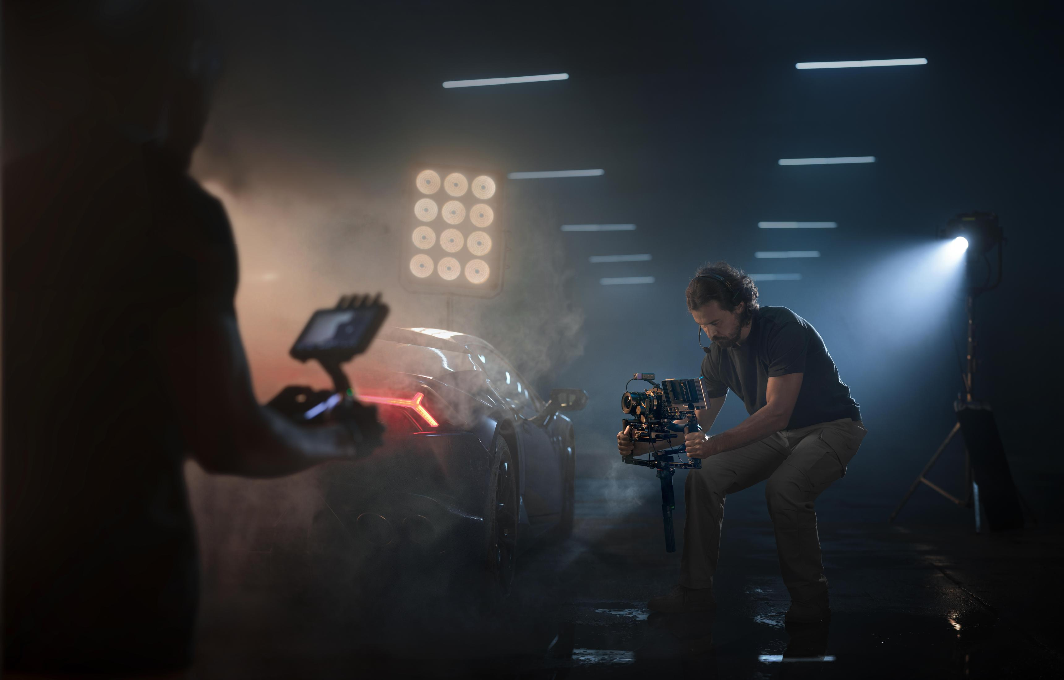 Filmen eines Autos. Zwei Personen, eine mit Kamera, die andere mit kleinem Bildschirm, in dunklem Studio.