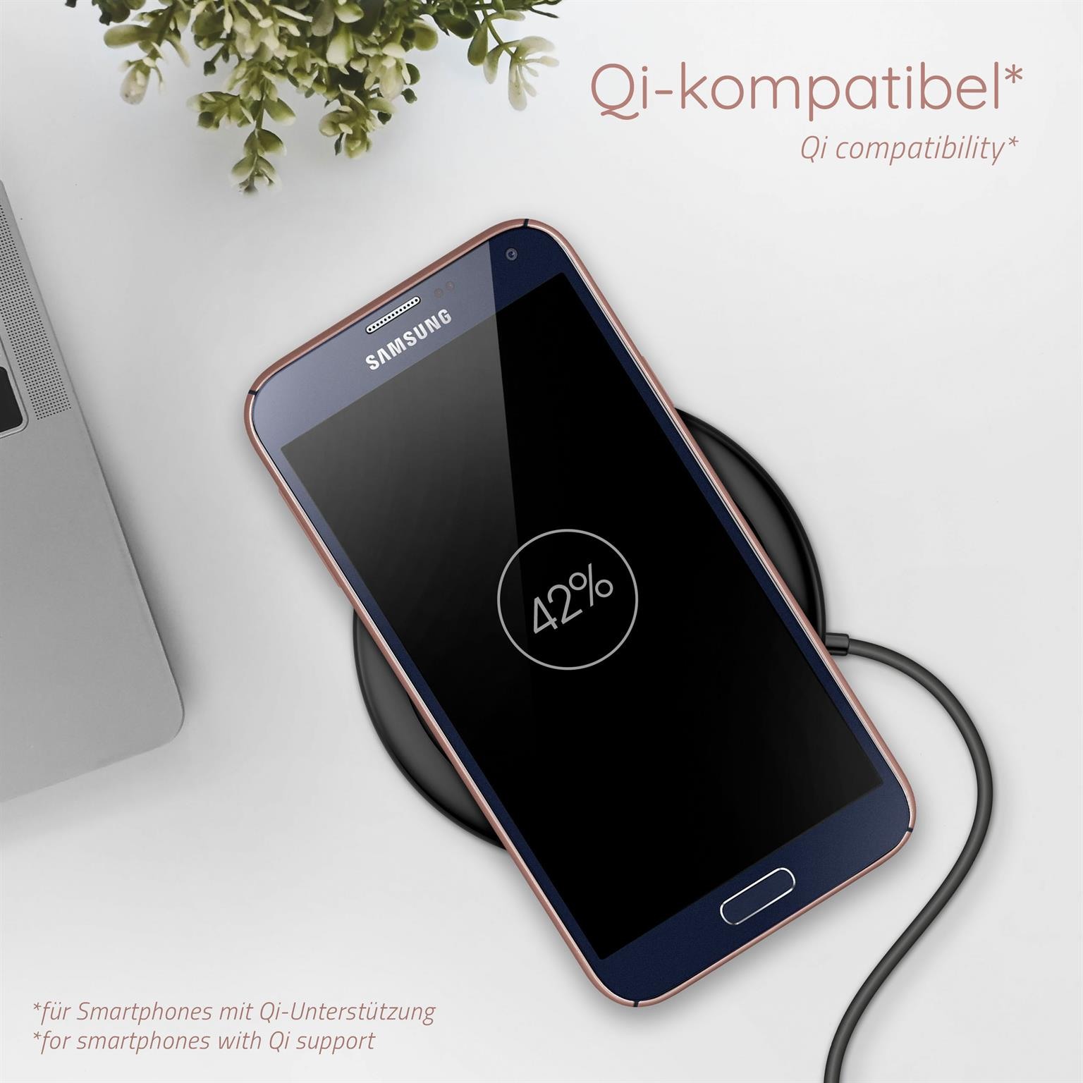 Ein Telefon auf einem kabellosen Ladegerät, zeigt 42%. Eine Pflanze und ein Laptop links. Der Text ist deutsch.