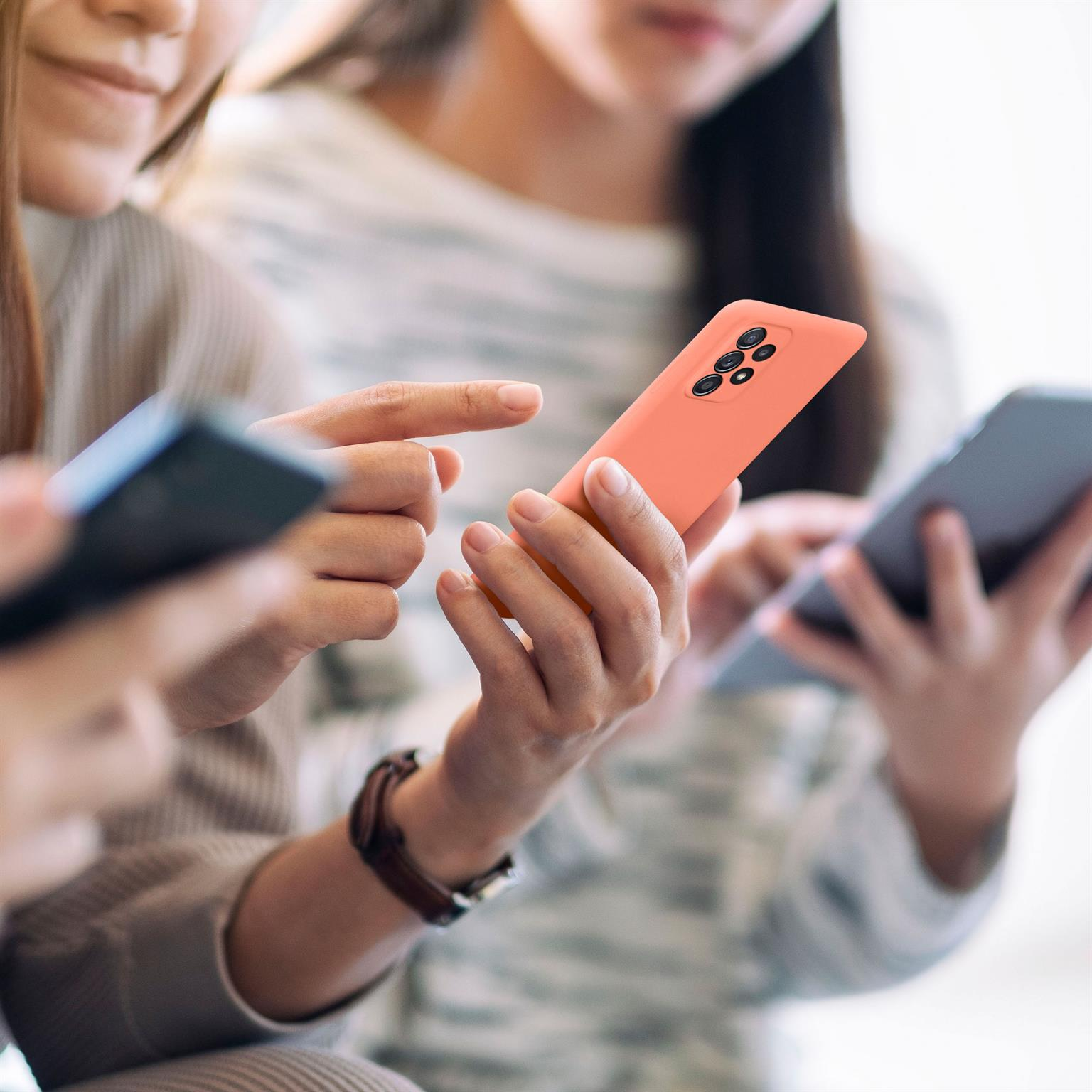 Drei Personen halten Smartphones. Ein korallenfarbenes Telefon steht im Fokus.