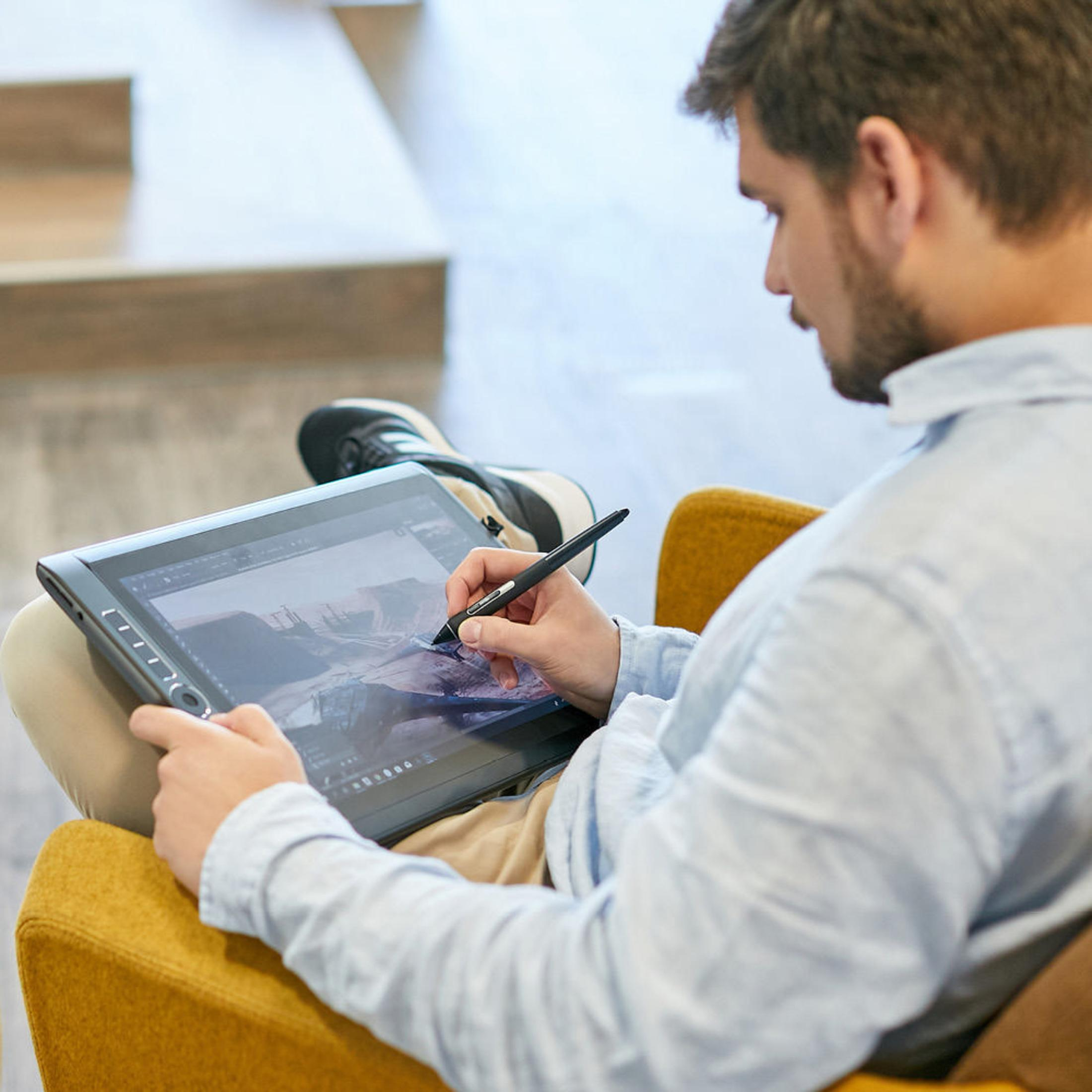 Ein Mann zeichnet sitzend auf einem Tablet mit einem Stift.