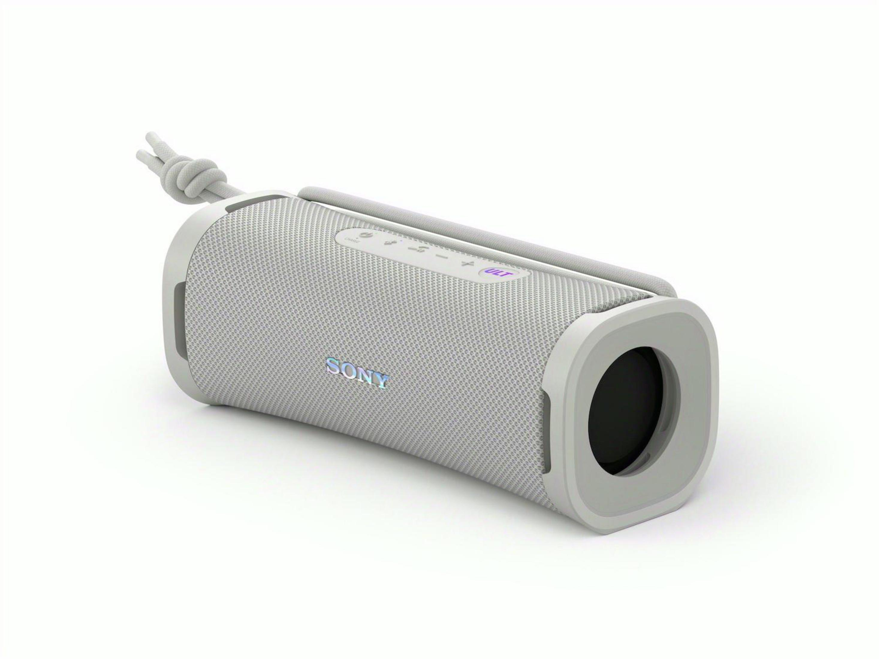 Altavoz cilíndrico gris con correa blanca sobre superficie blanca. Logo Sony al frente.