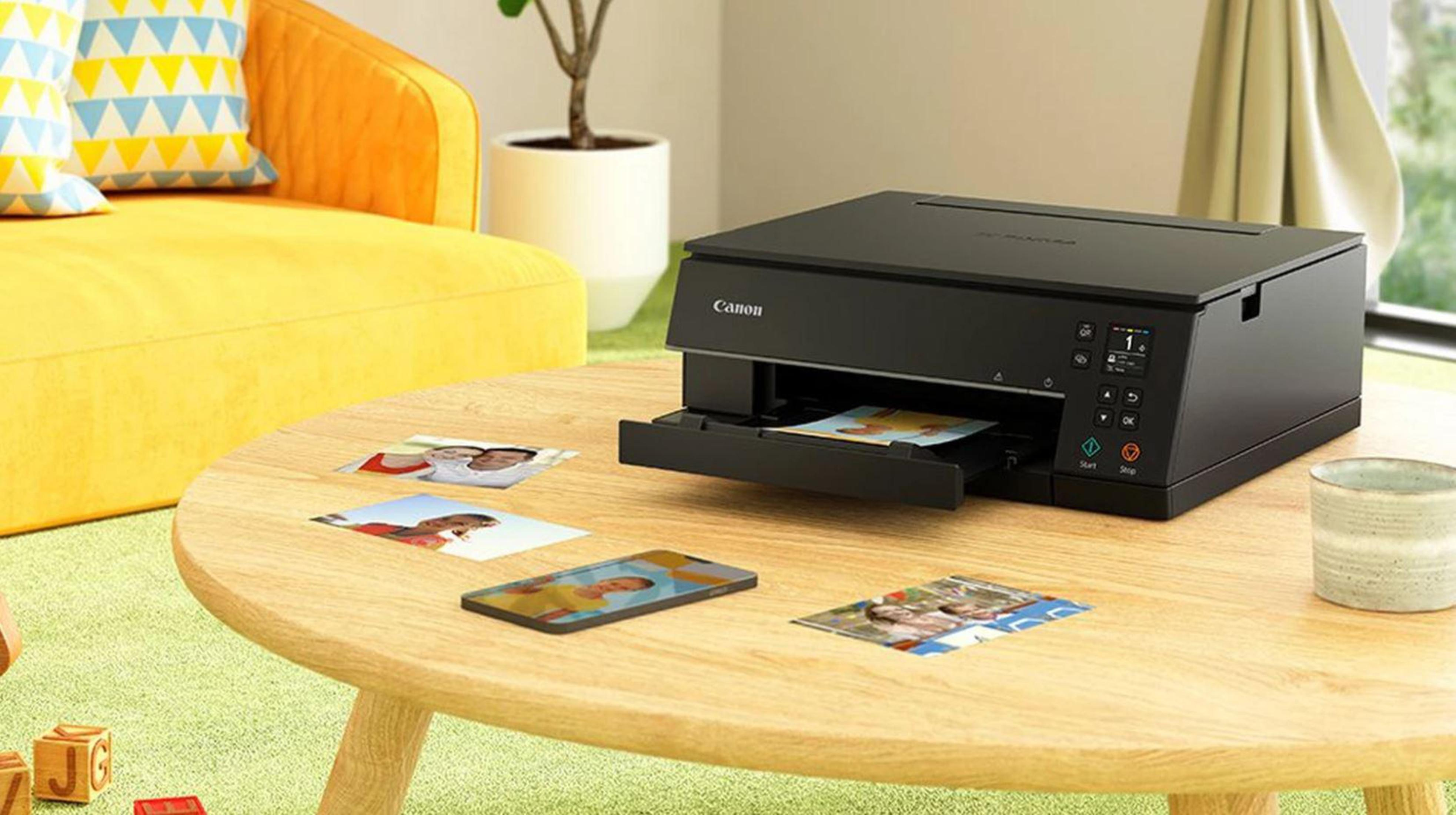 Czarna drukarka Canon na drewnianym stole ze zdjęciami i zielonym kubkiem. Scena wnętrza.