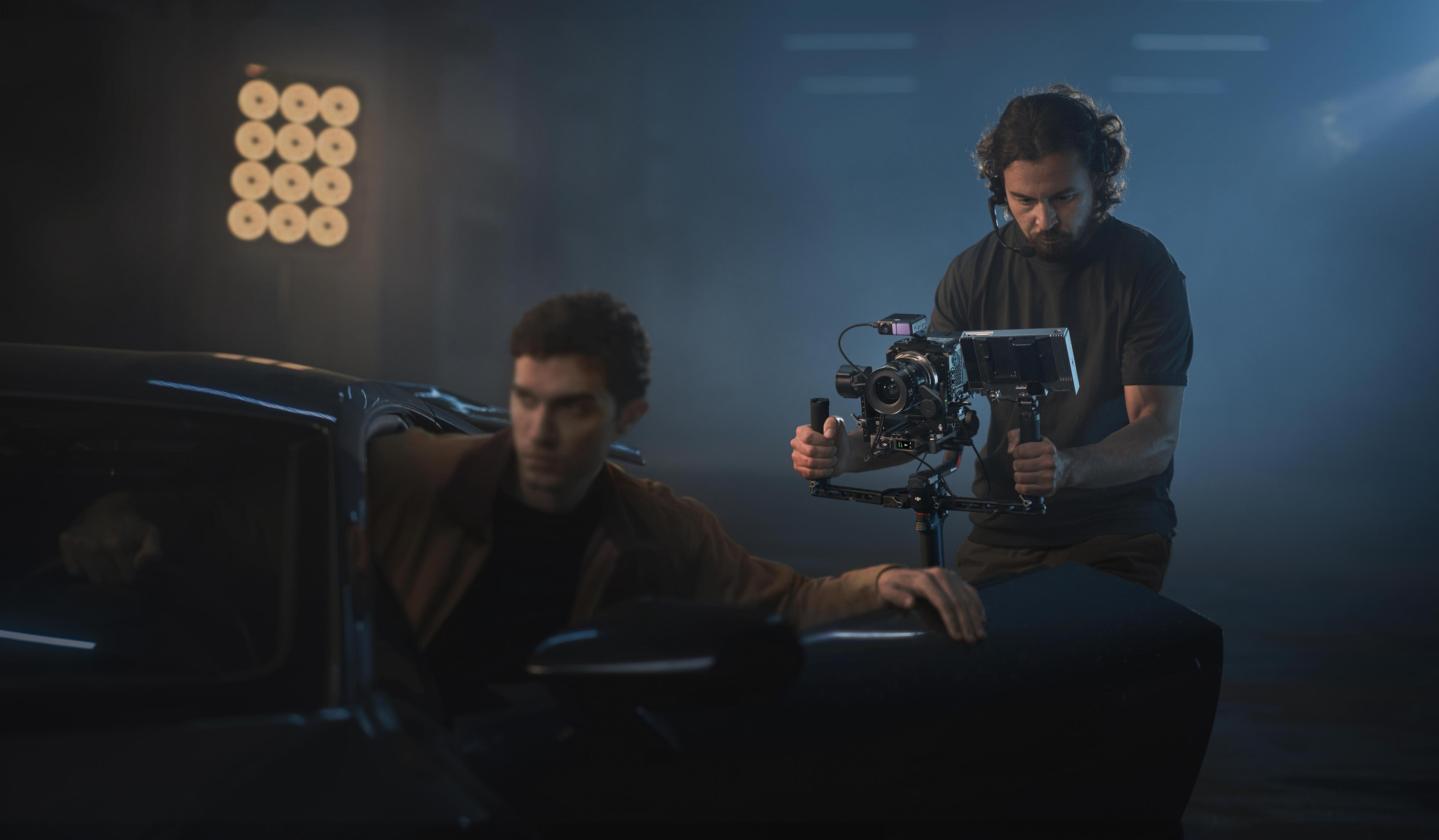 Ein Filmteam dreht einen Mann, der in einer dunklen, blau beleuchteten Umgebung aus einem Auto steigt.