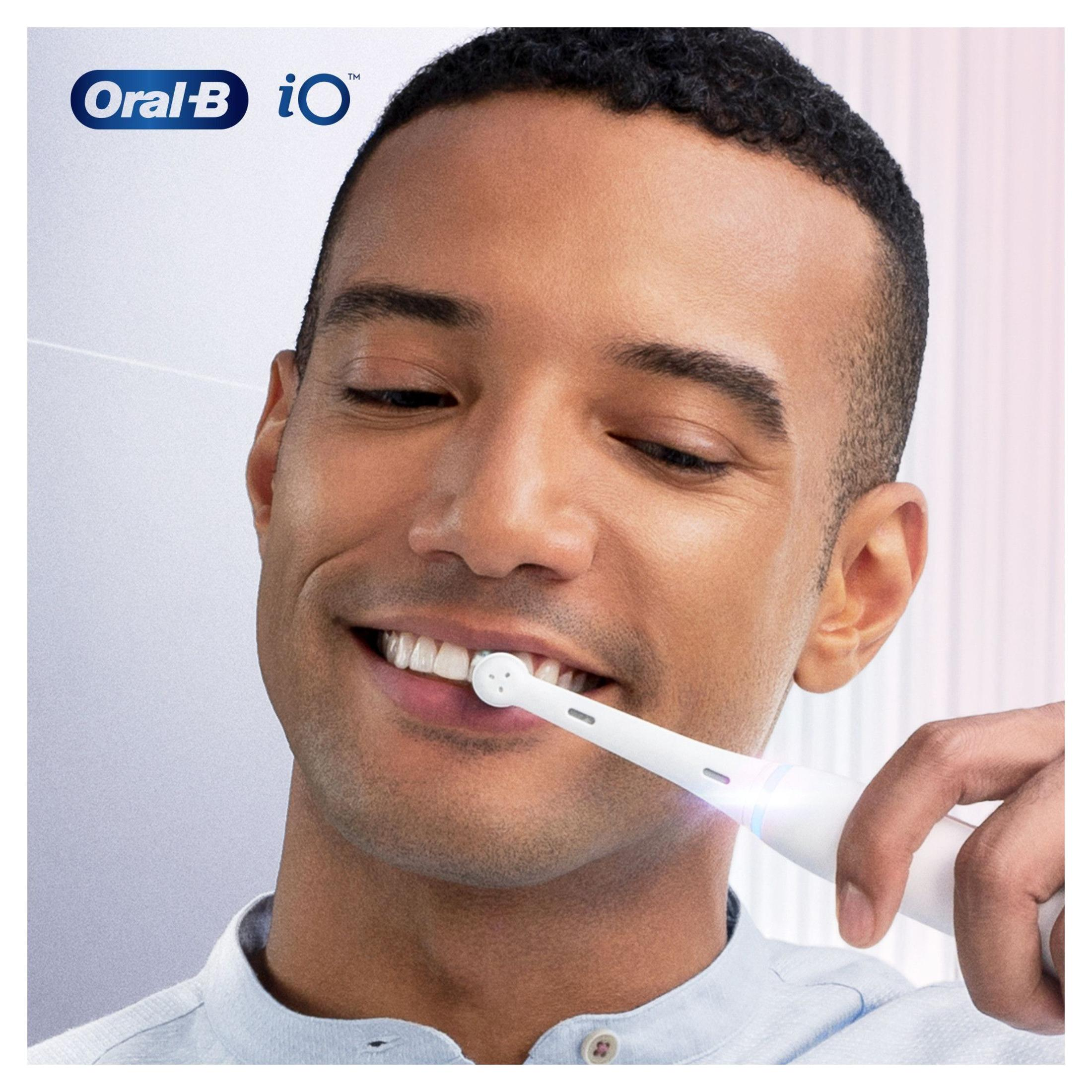 Mann putzt Zähne mit Oral-B iO elektrischer Zahnbürste, lächelnd, weißer Hintergrund.