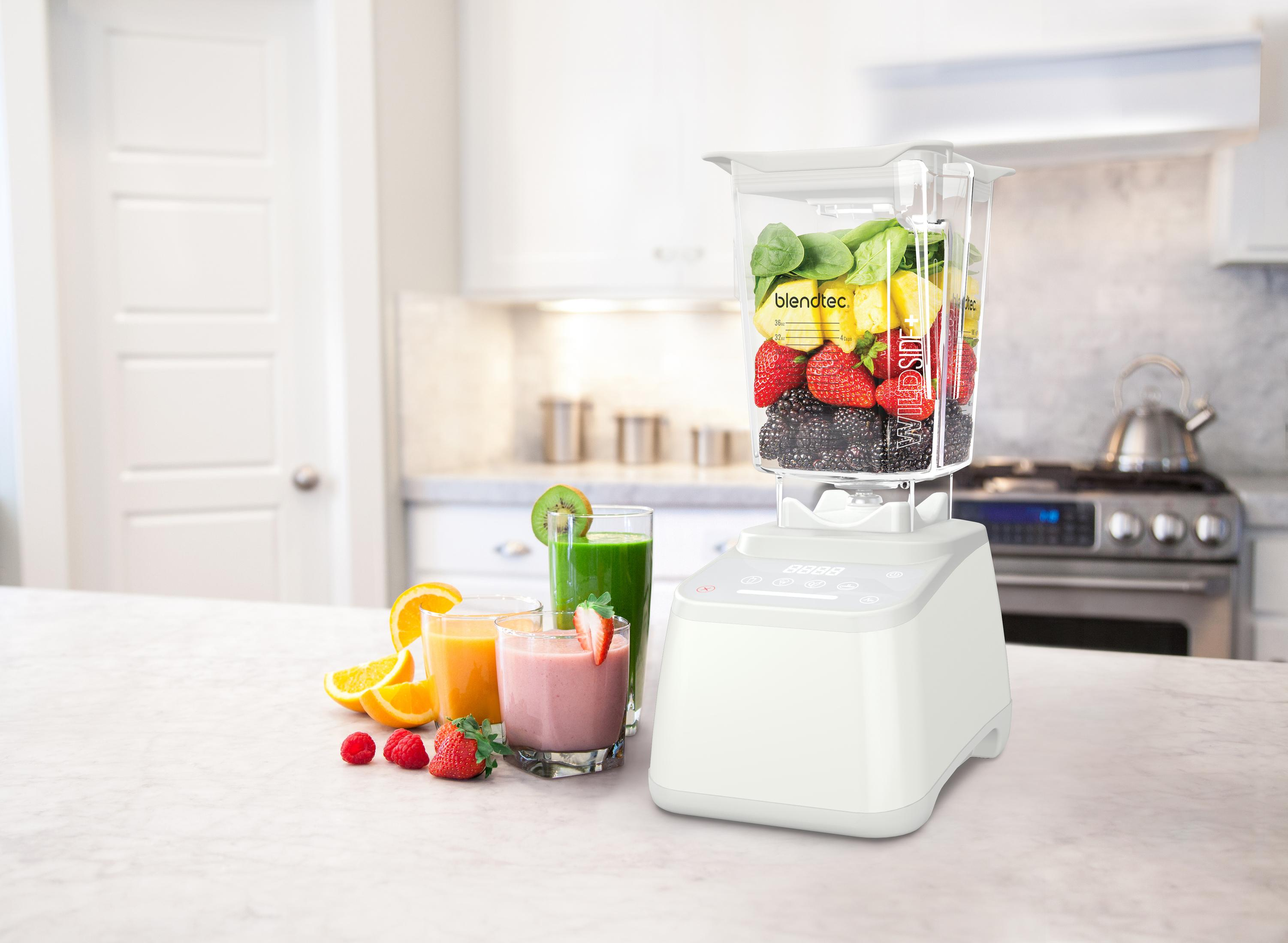 Una licuadora con frutas y verduras dentro, y tres vasos de batidos cerca en una encimera.