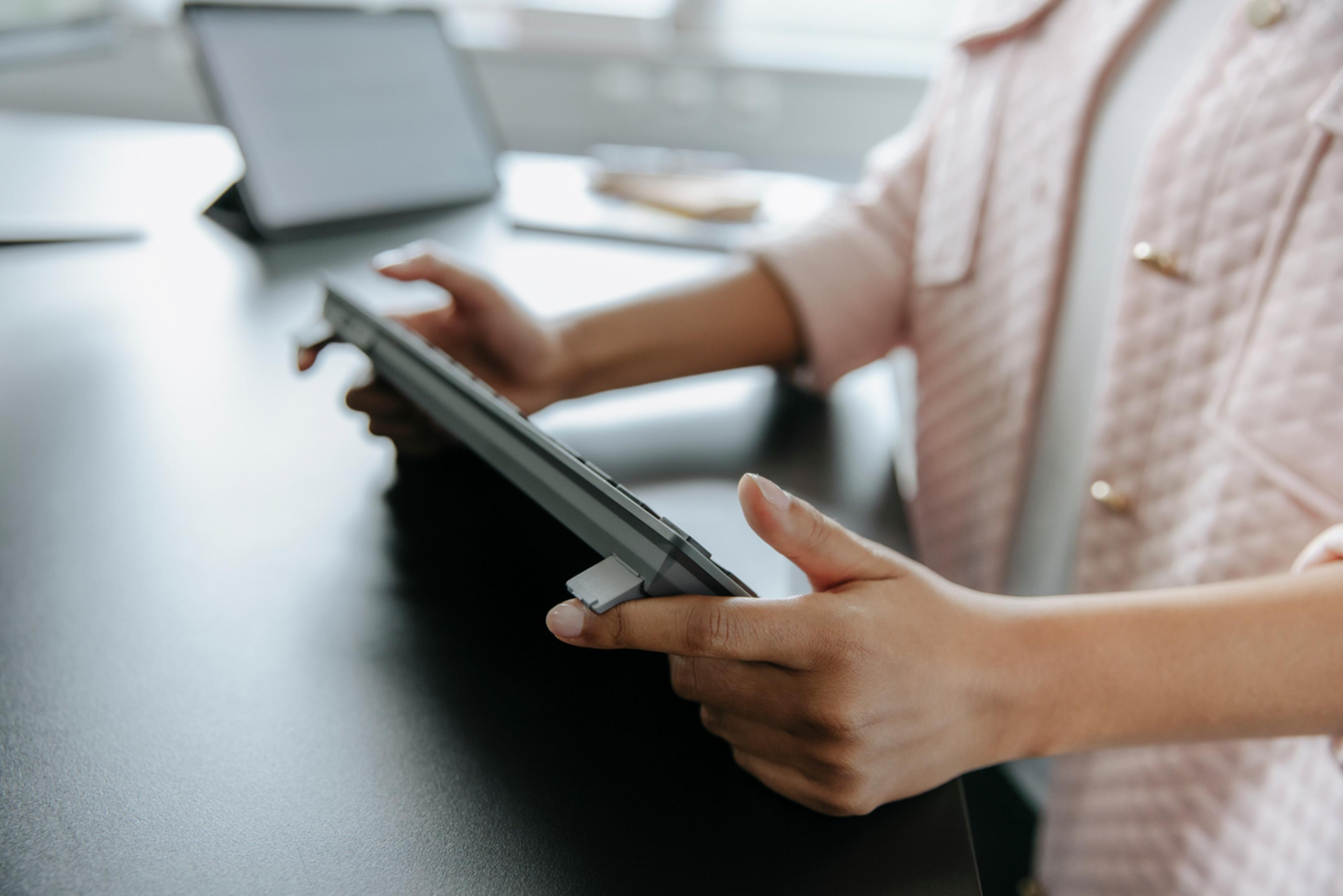 Une femme tenant un clavier gris dans ses mains au-dessus d'un bureau noir. Fond blanc.