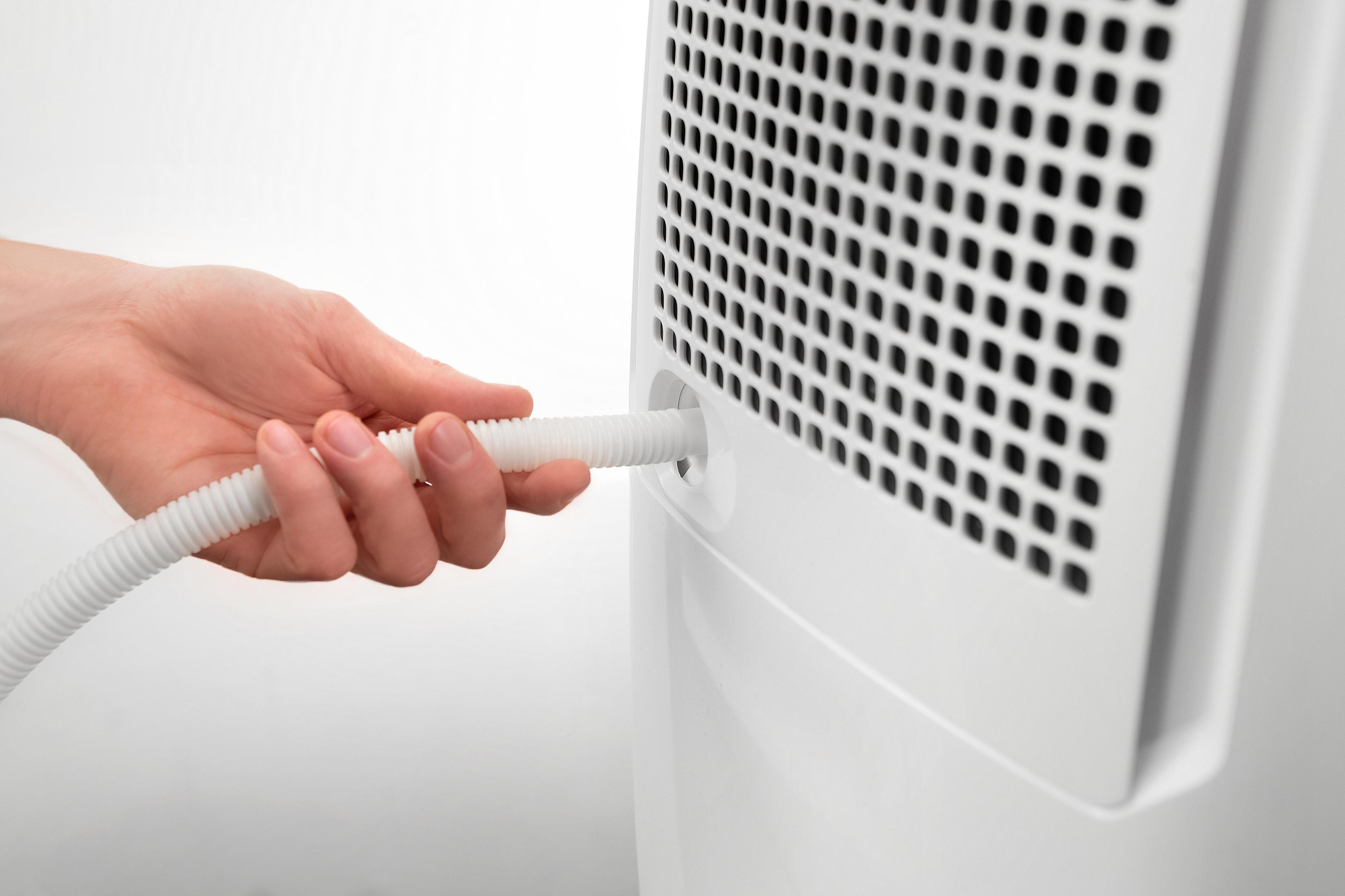 Ręka podłączająca biały wąż do białego urządzenia. Urządzenie ma czarny otwór wentylacyjny.