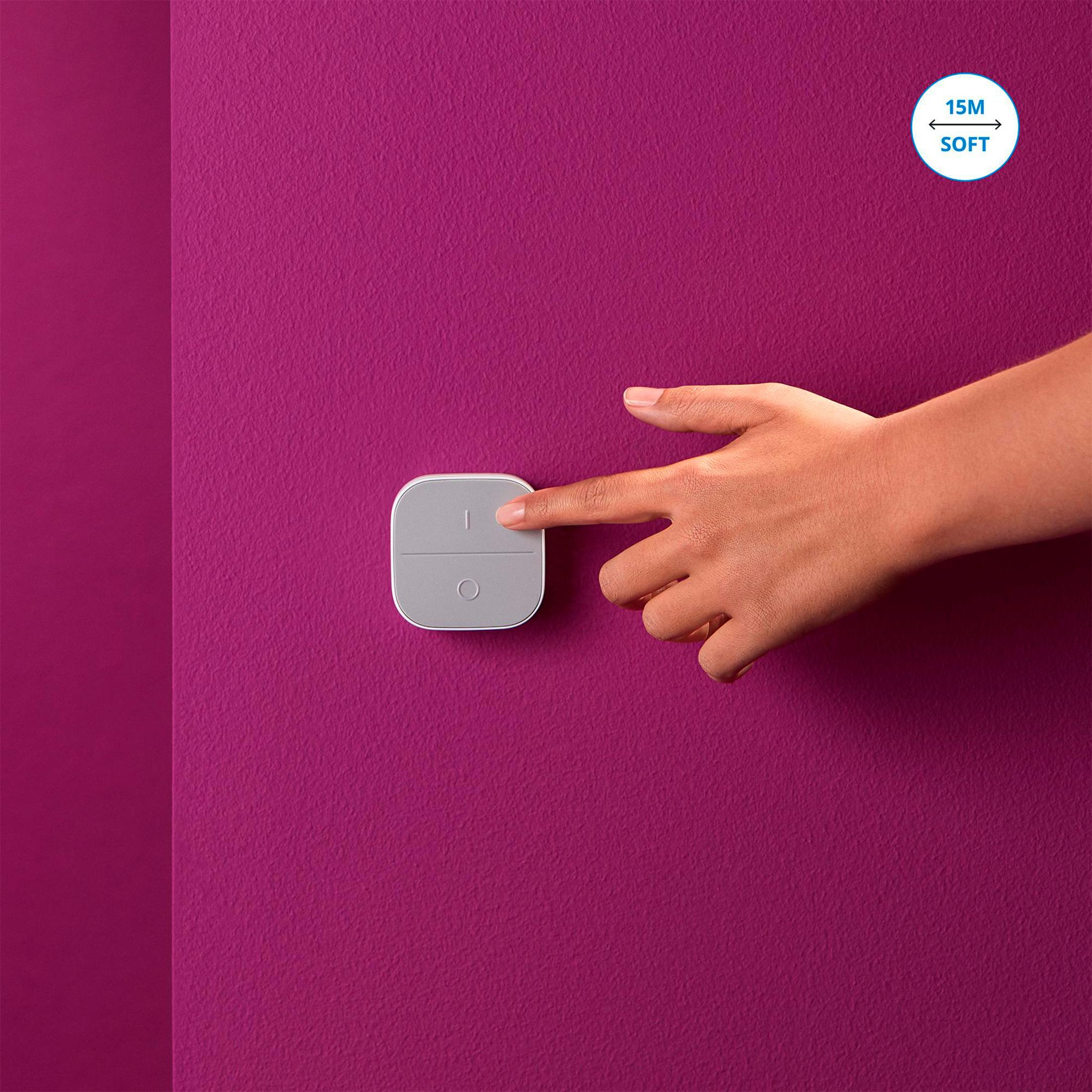 Hand drukt op een witte knop op een grijze muur. De muur is paars. Tekst: '15M SOFT'.