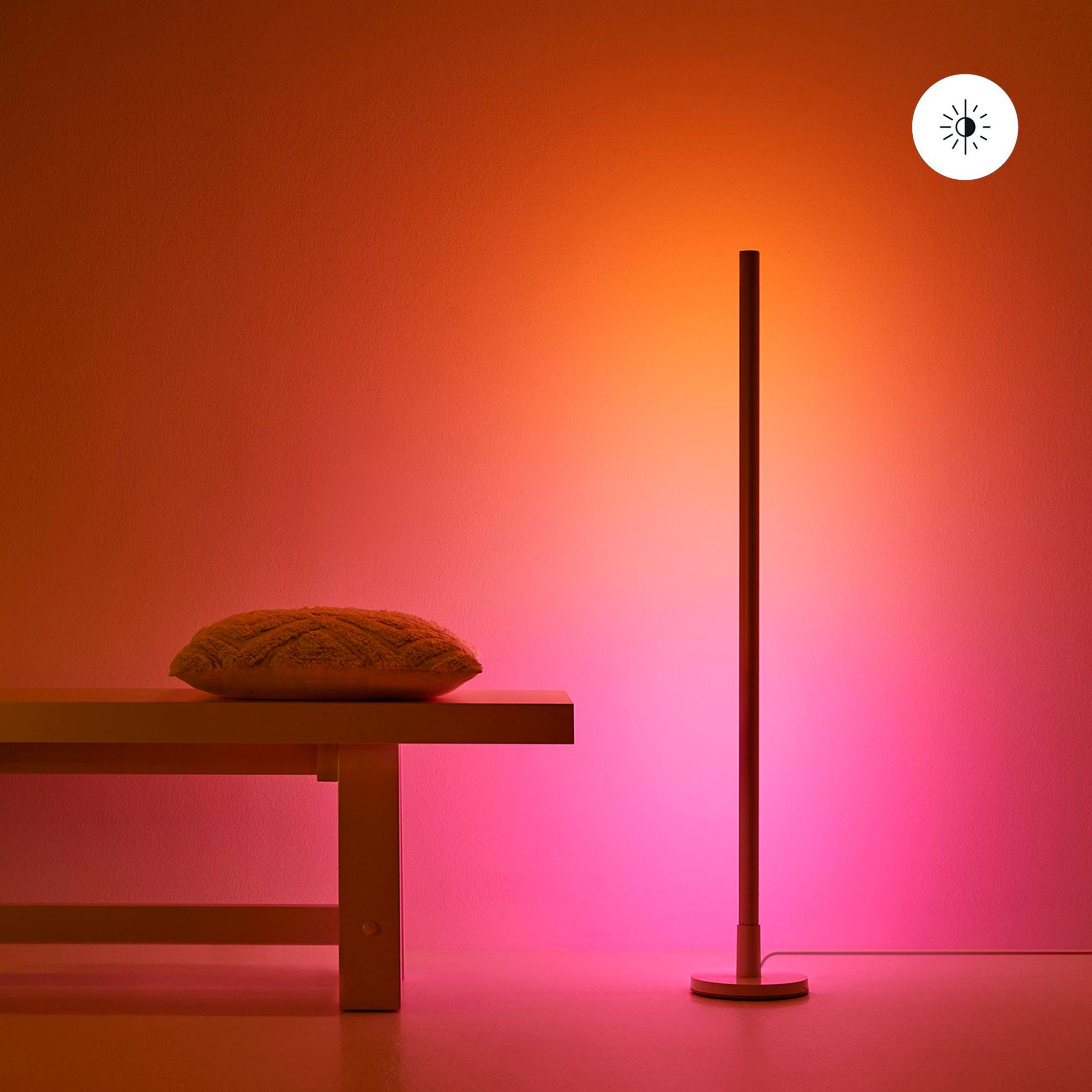 Hoge, verlichte vloerlamp tegen een gradiëntmuur. Een bank met kussen.