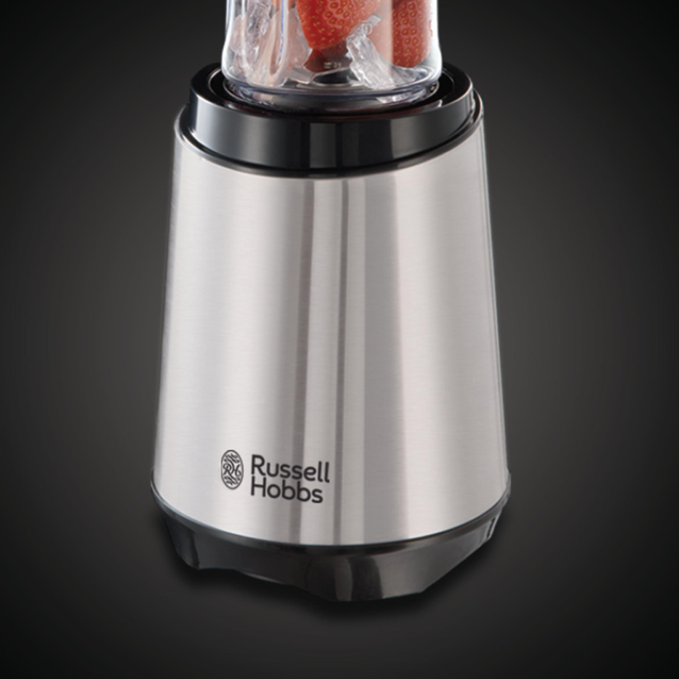 Licuadora con fresas dentro de un recipiente transparente. Cuerpo metálico, base negra.