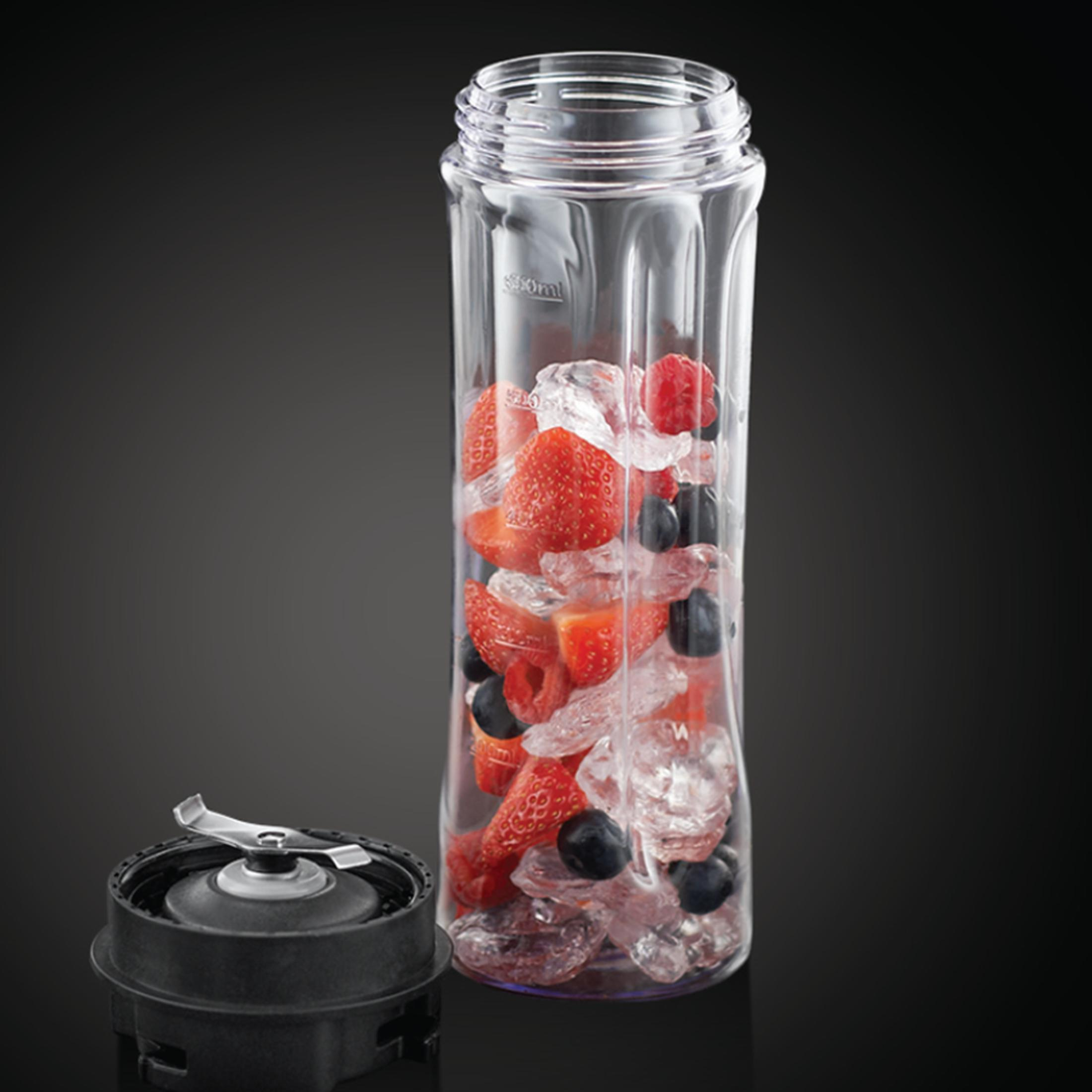 Botella de licuadora transparente llena de hielo, fresas y arándanos, con una cuchilla.