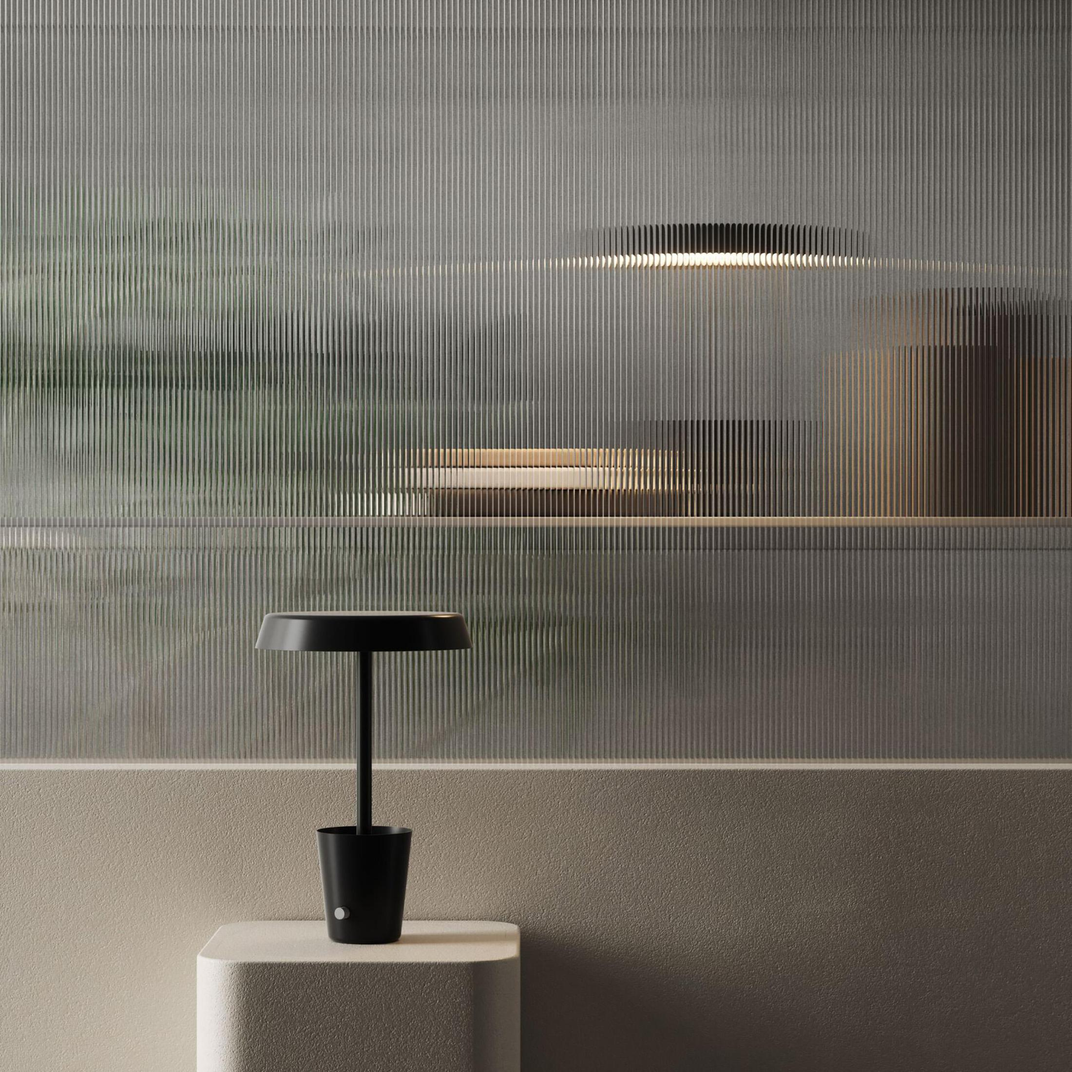 Lampada da scrivania nera su supporto bianco. Parete in vetro strutturato con illuminazione soffusa.