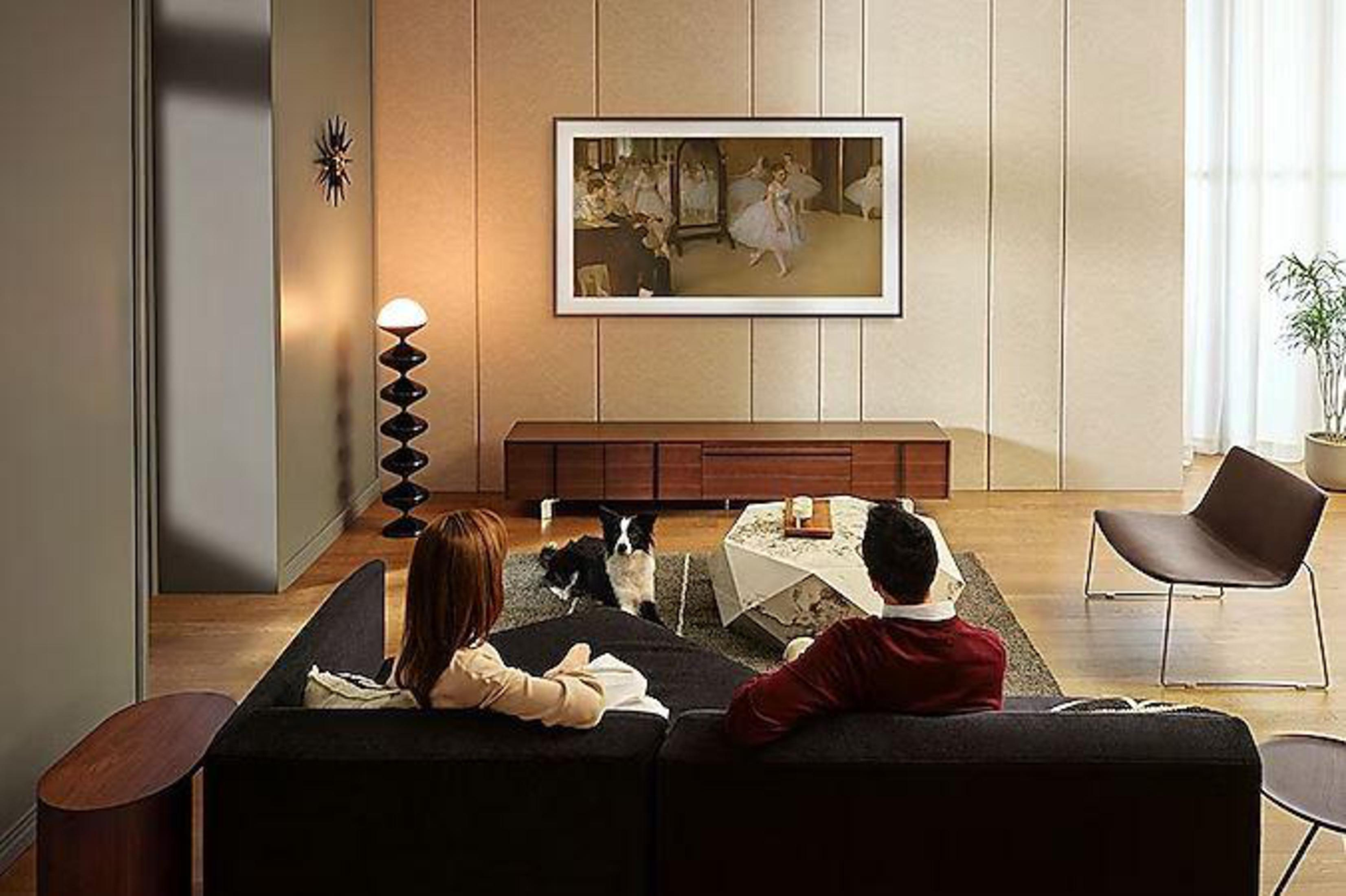 Ludzie na czarnej sofie oglądający telewizję z psem.