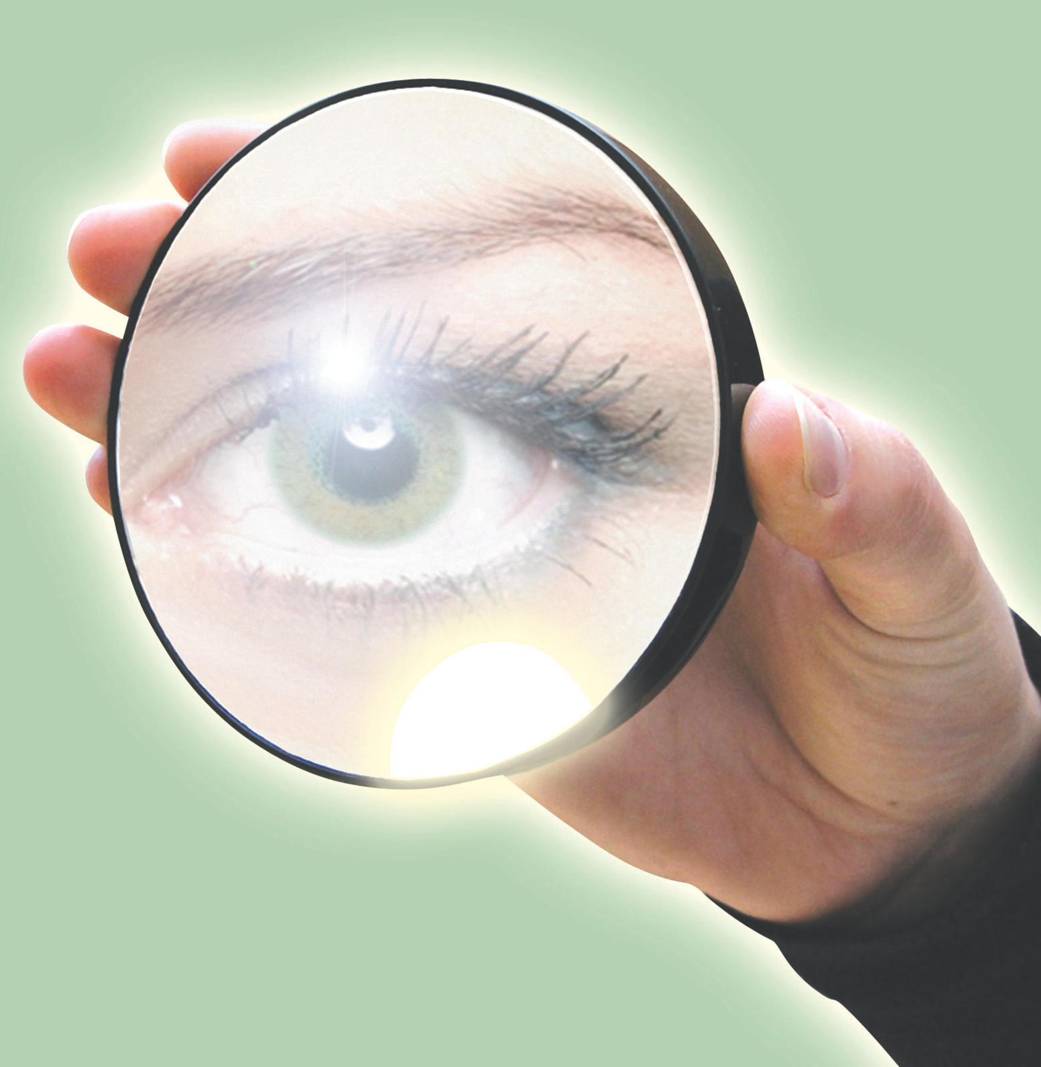 Hand hält Lupe über einem Auge. Das Auge spiegelt sich im Glas.