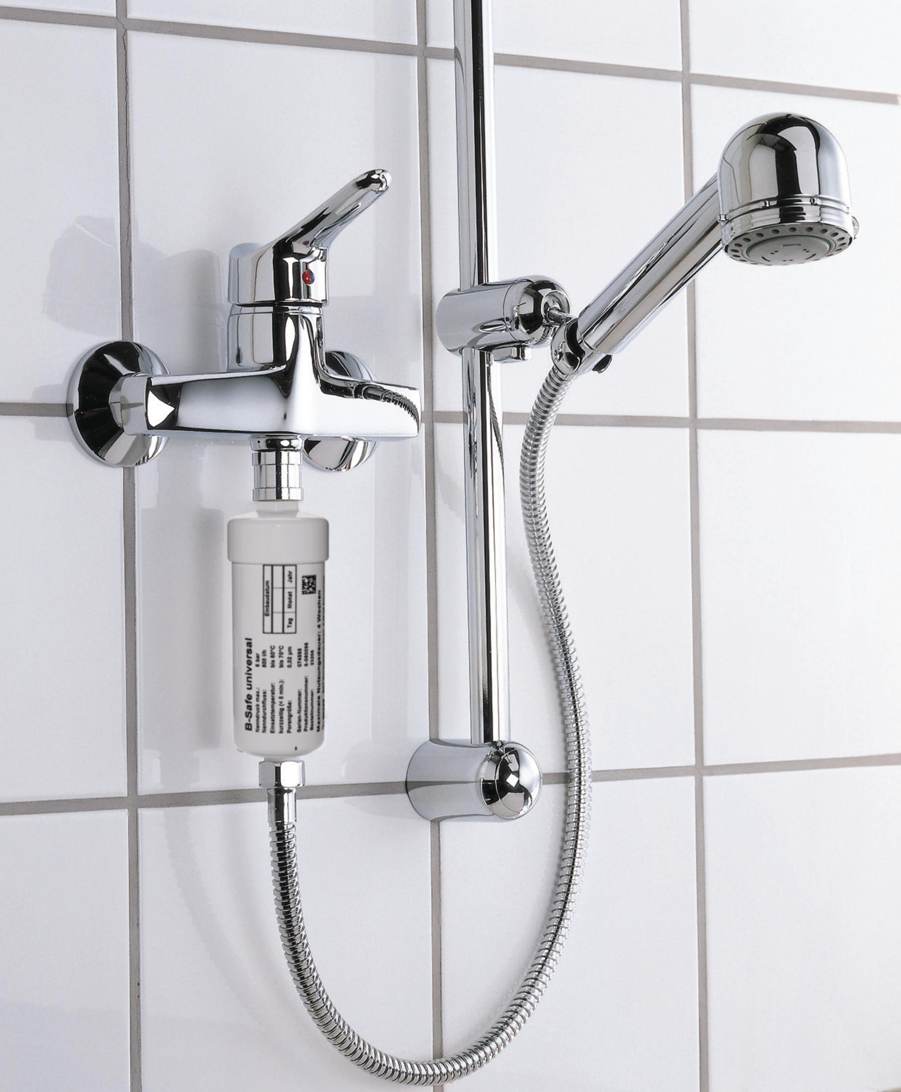 Chromowana bateria prysznicowa z filtrem i słuchawką, białe tło z płytek.