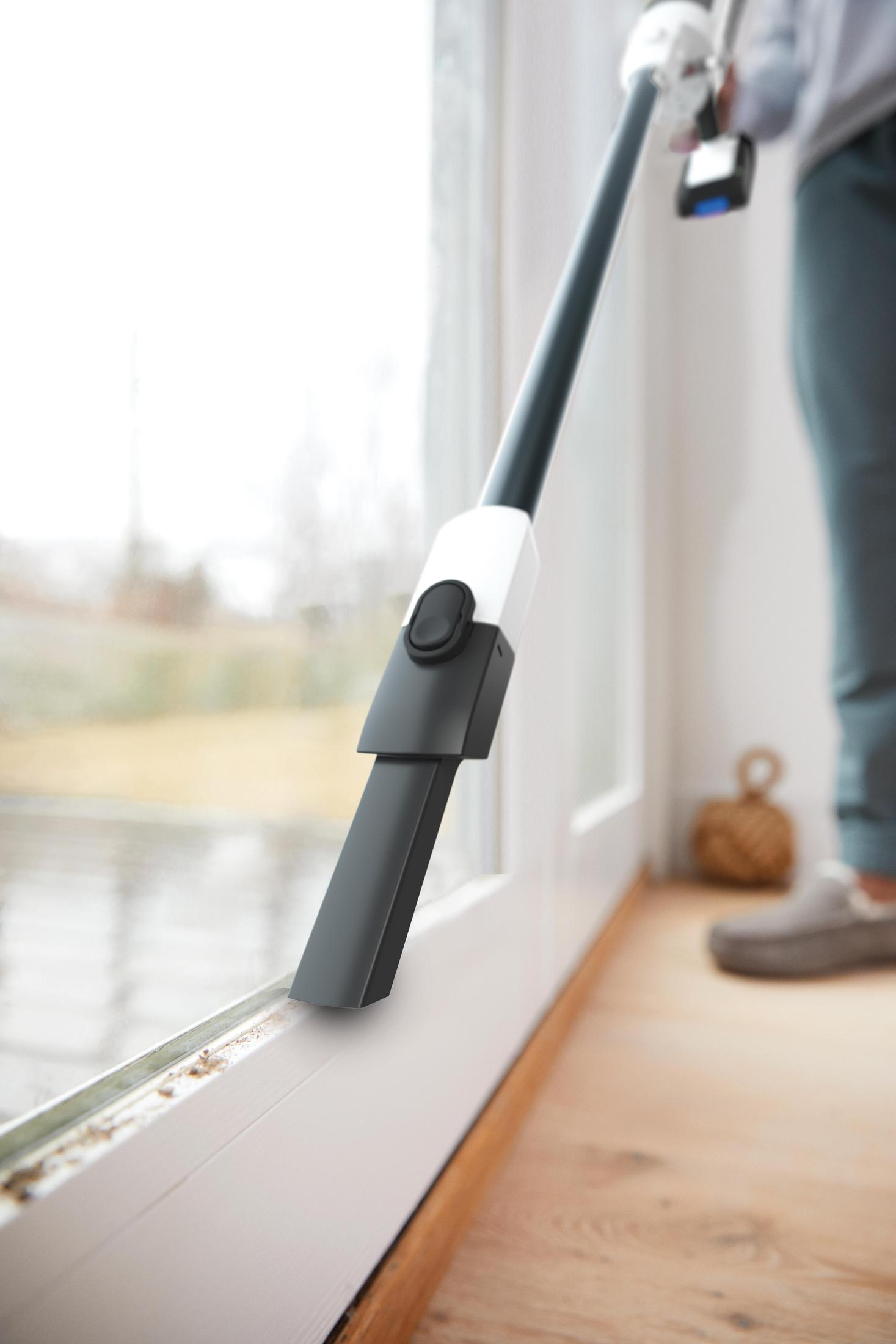 Person reinigt einen Fensterrahmen mit einem Staubsauger. Fenster und unscharfer Hintergrund.