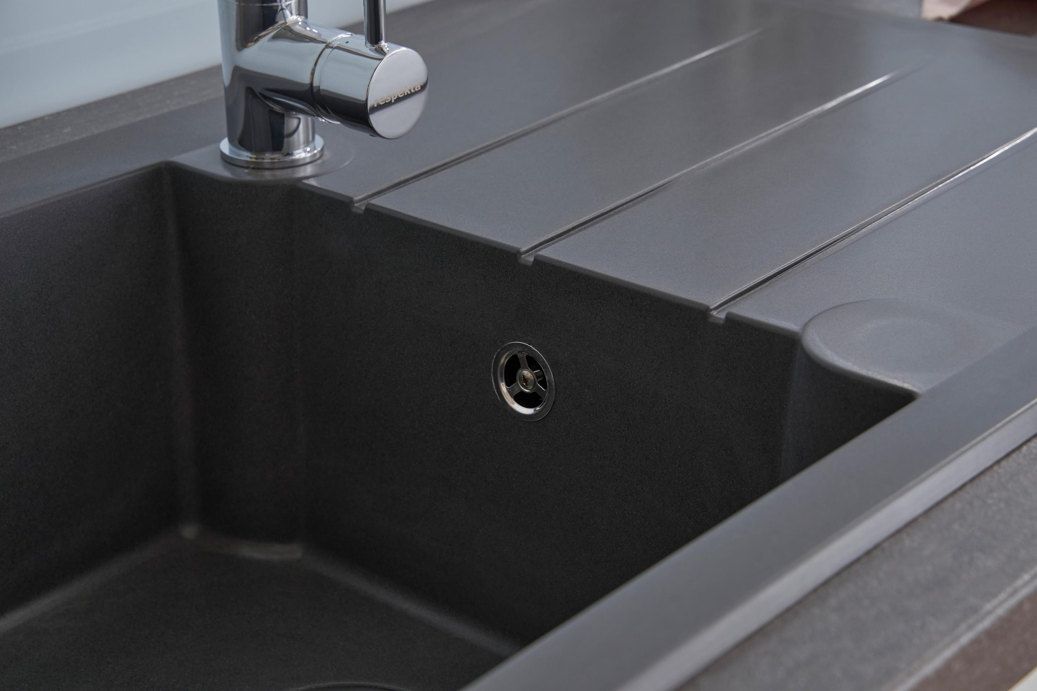 Nahaufnahme eines Küchenbeckens. Dunkelgraue Farbe. Wasserhahn und Abfluss sichtbar.